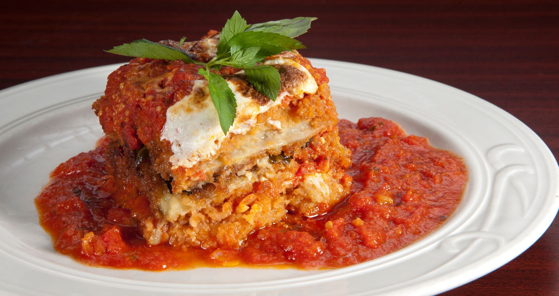 Lasagna-like dish on a white plate with tomato sauce, garnished with basil leaves.