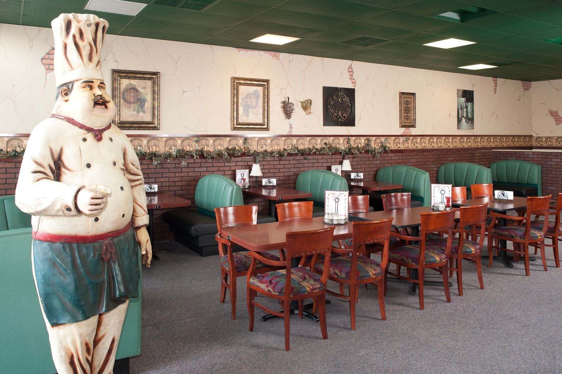 Restaurant interior: large chef statue, booths, wooden tables and chairs, decorative wall art.