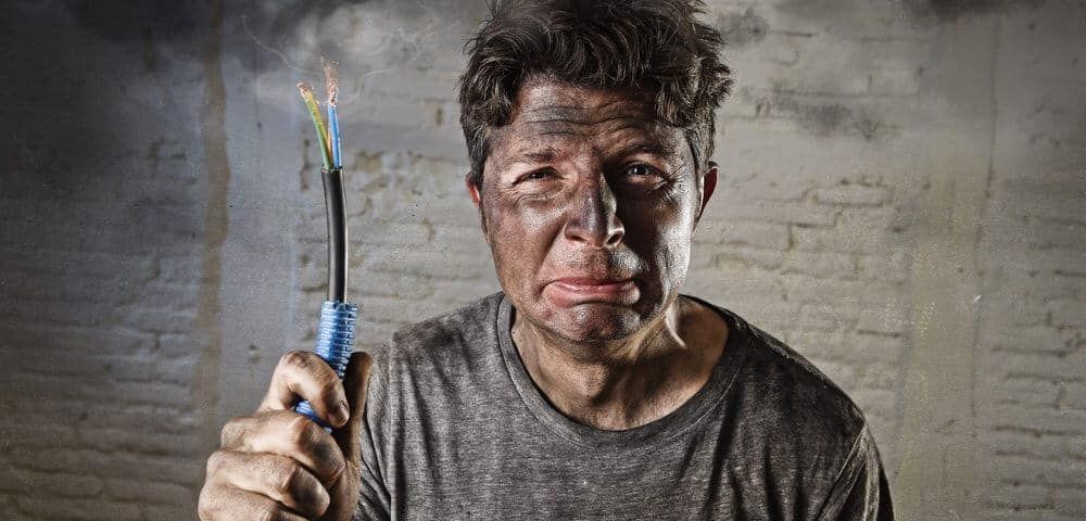 A man with a dirty face is holding a screwdriver in front of a brick wall.