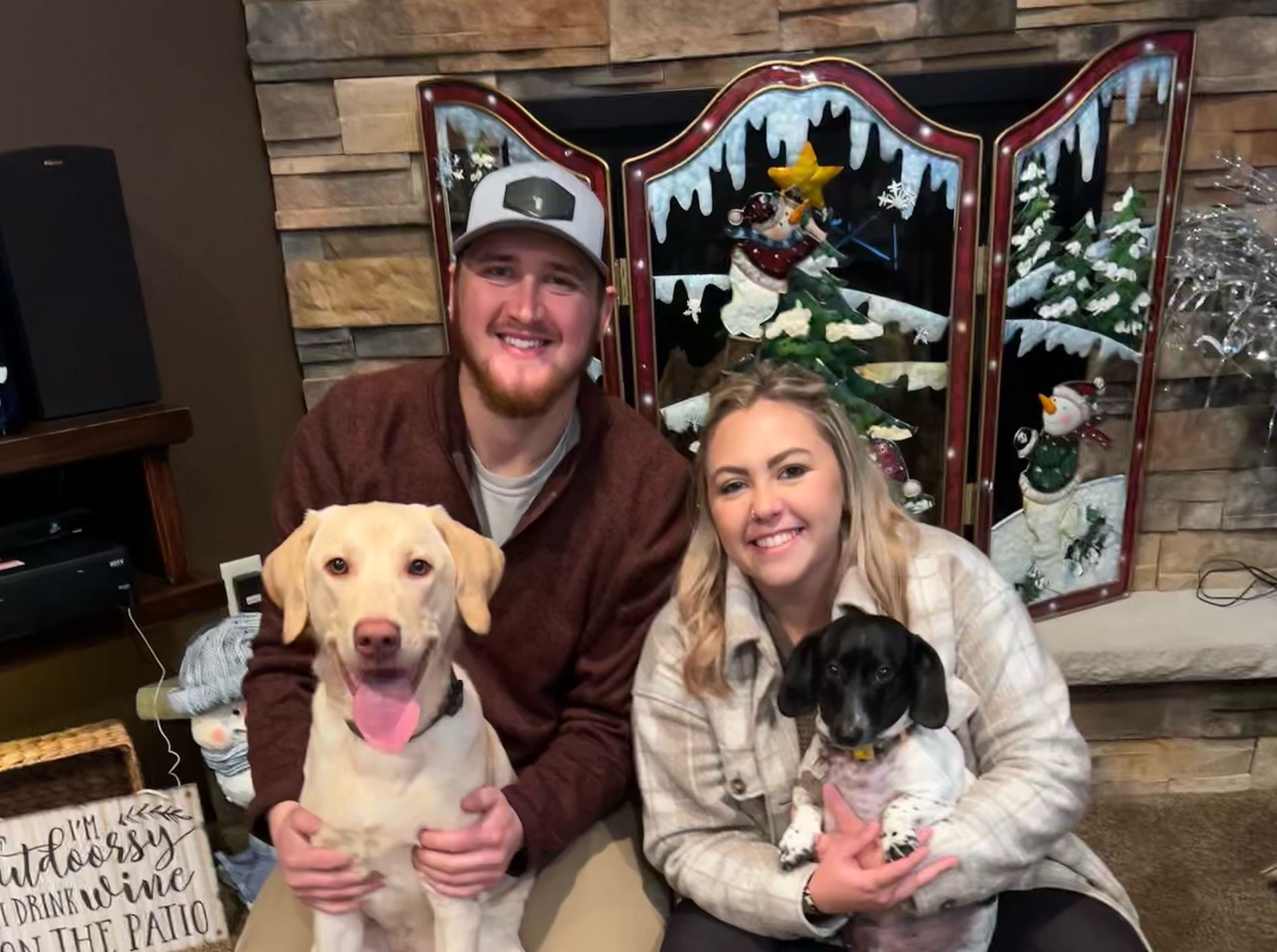 A man and a woman are holding a dog in front of a fireplace.