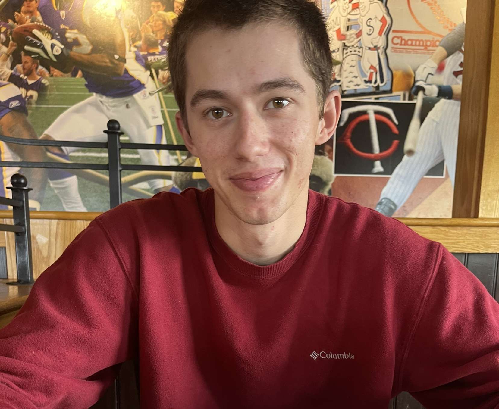 A young man in a red sweater is sitting at a table in a restaurant.