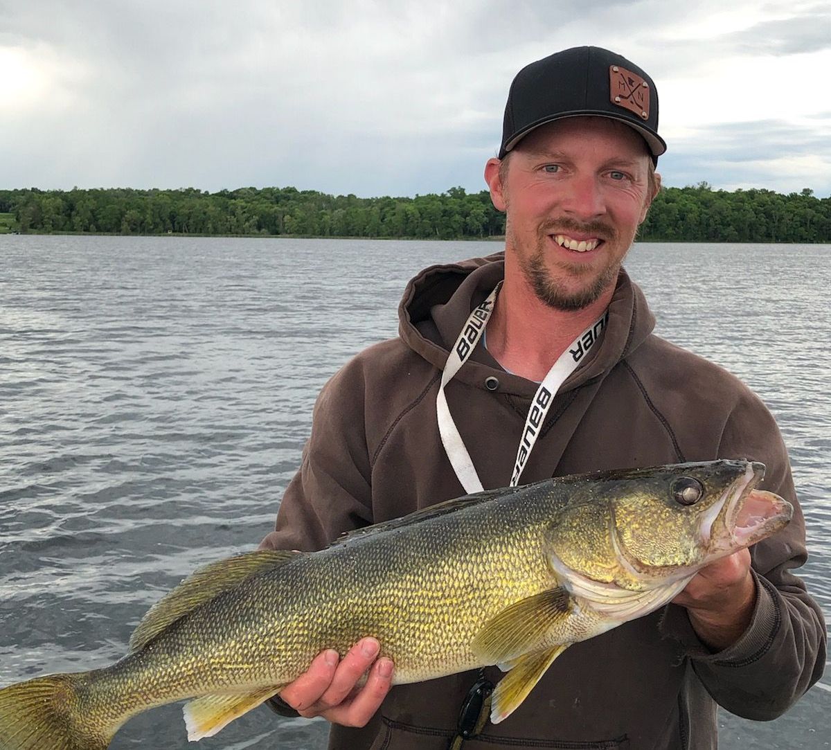 A man is holding a large fish in his hands in front of a lake.