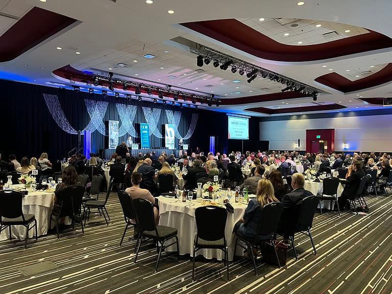 Banquet hall with guests seated at round tables during a formal event, stage lit in blue at the front