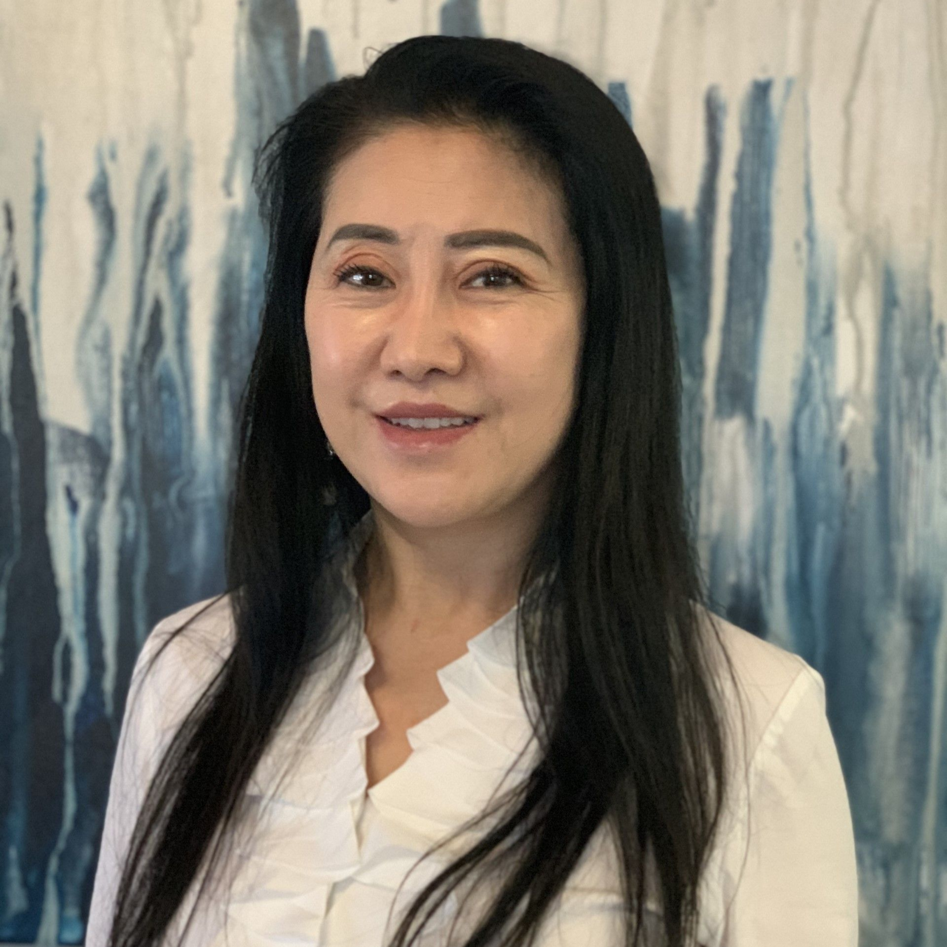 Woman with long dark hair in a white blouse standing before an abstract blue-gray painting