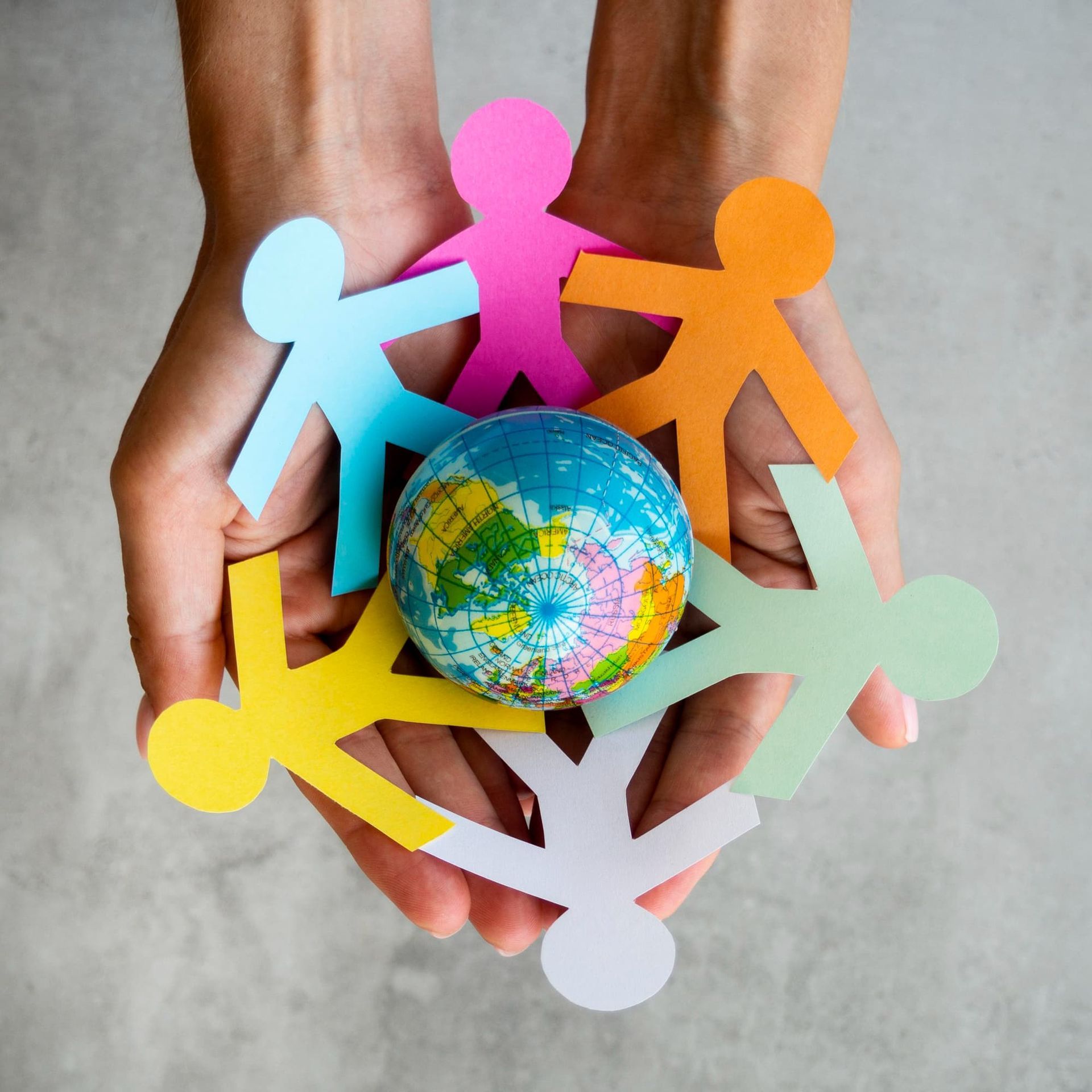 Mãos segurando um globo terrestre rodeado por figuras de papel coloridas, simbolizando a comunidade e a união global.