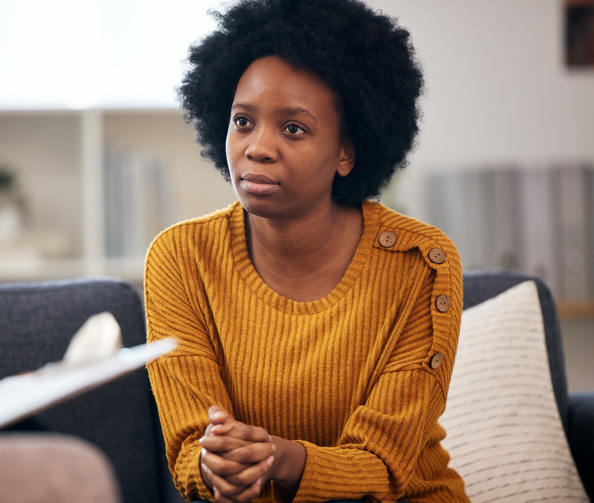 Woman in yellow sweater sits on couch, looking toward a person off-screen. Woman in yellow sweater sits on couch, looking toward a person off-screen.
