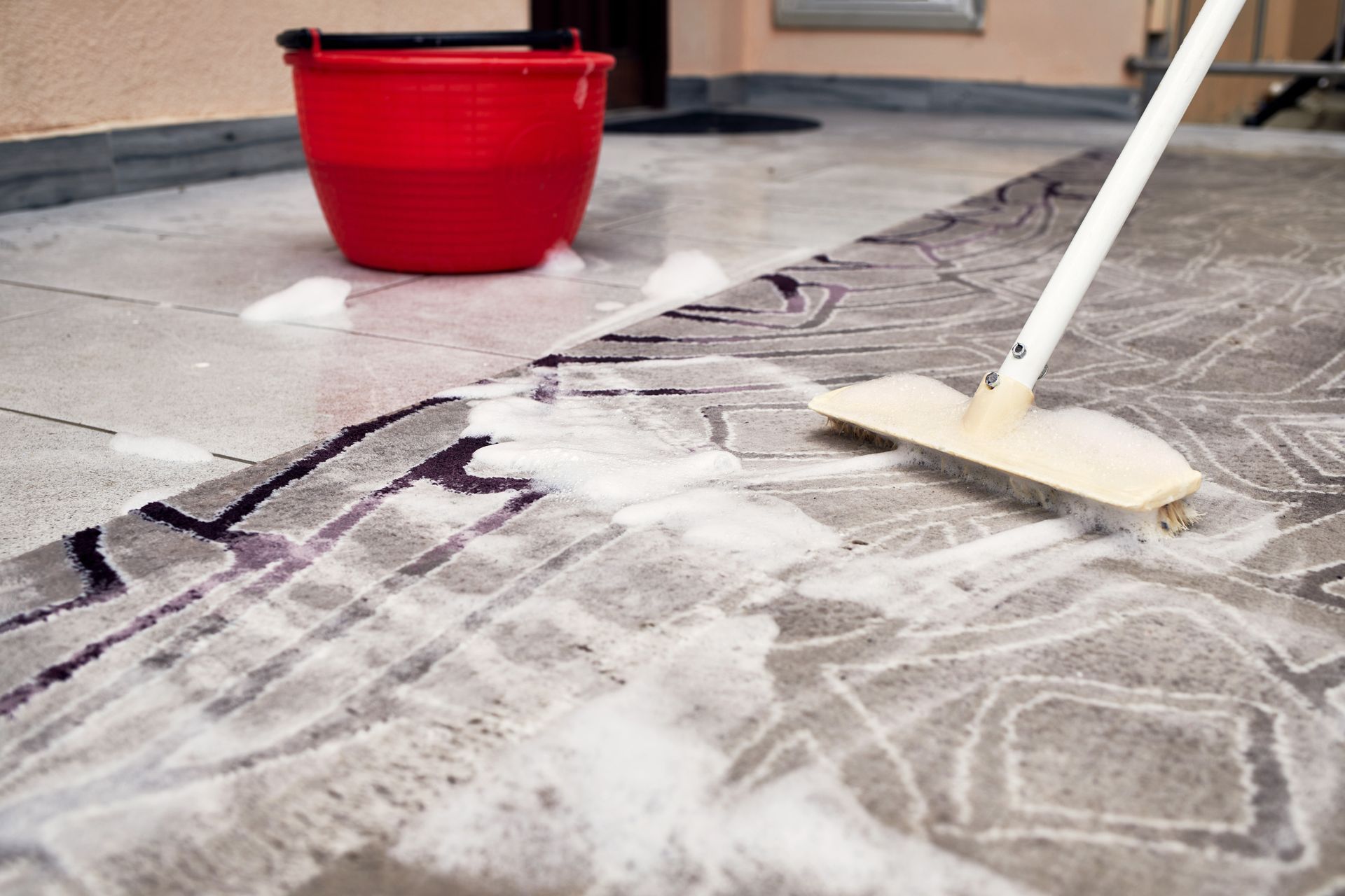 Person mopping a soapy tiled floor with a red bucket nearby