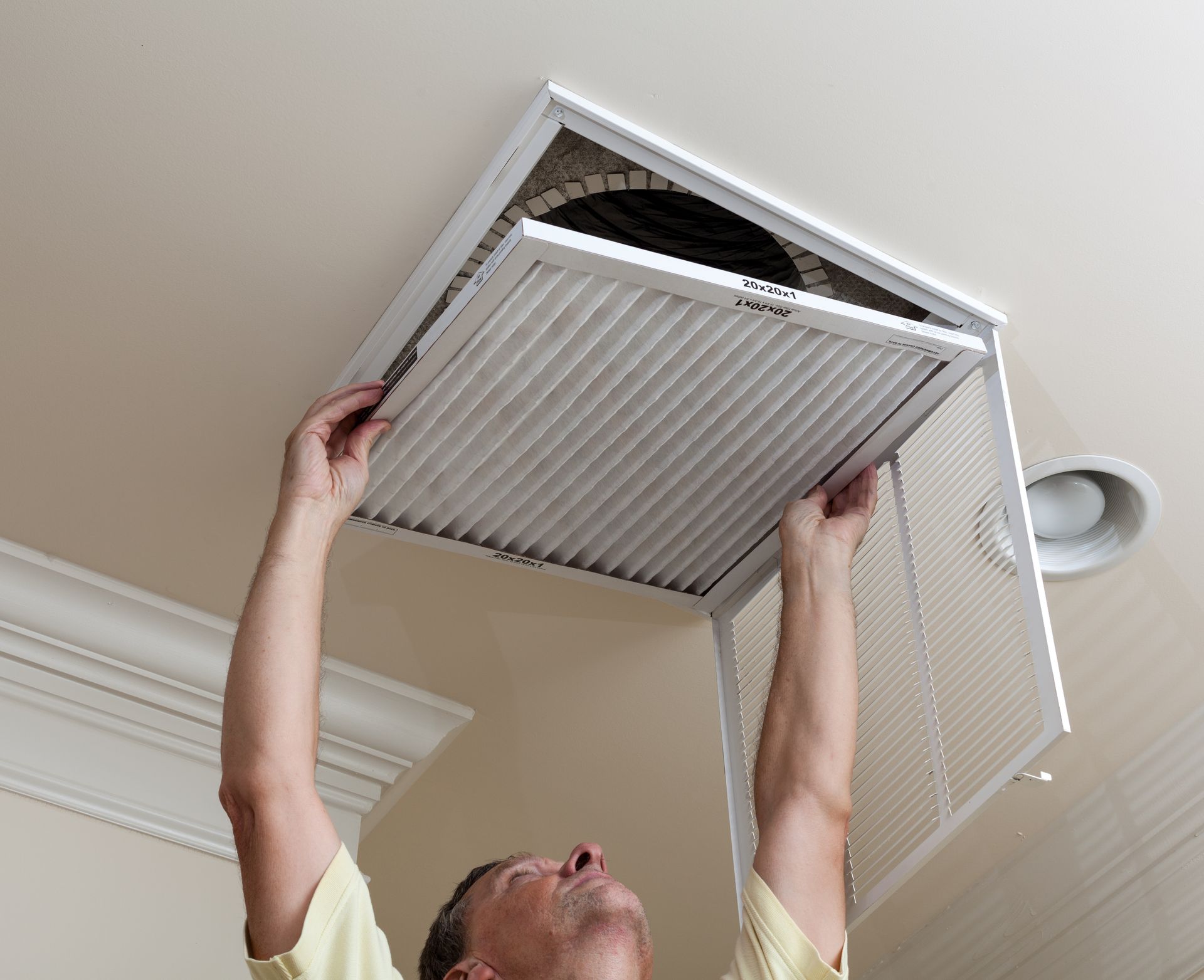 Man changing a ceiling air filter in a white vent panel.