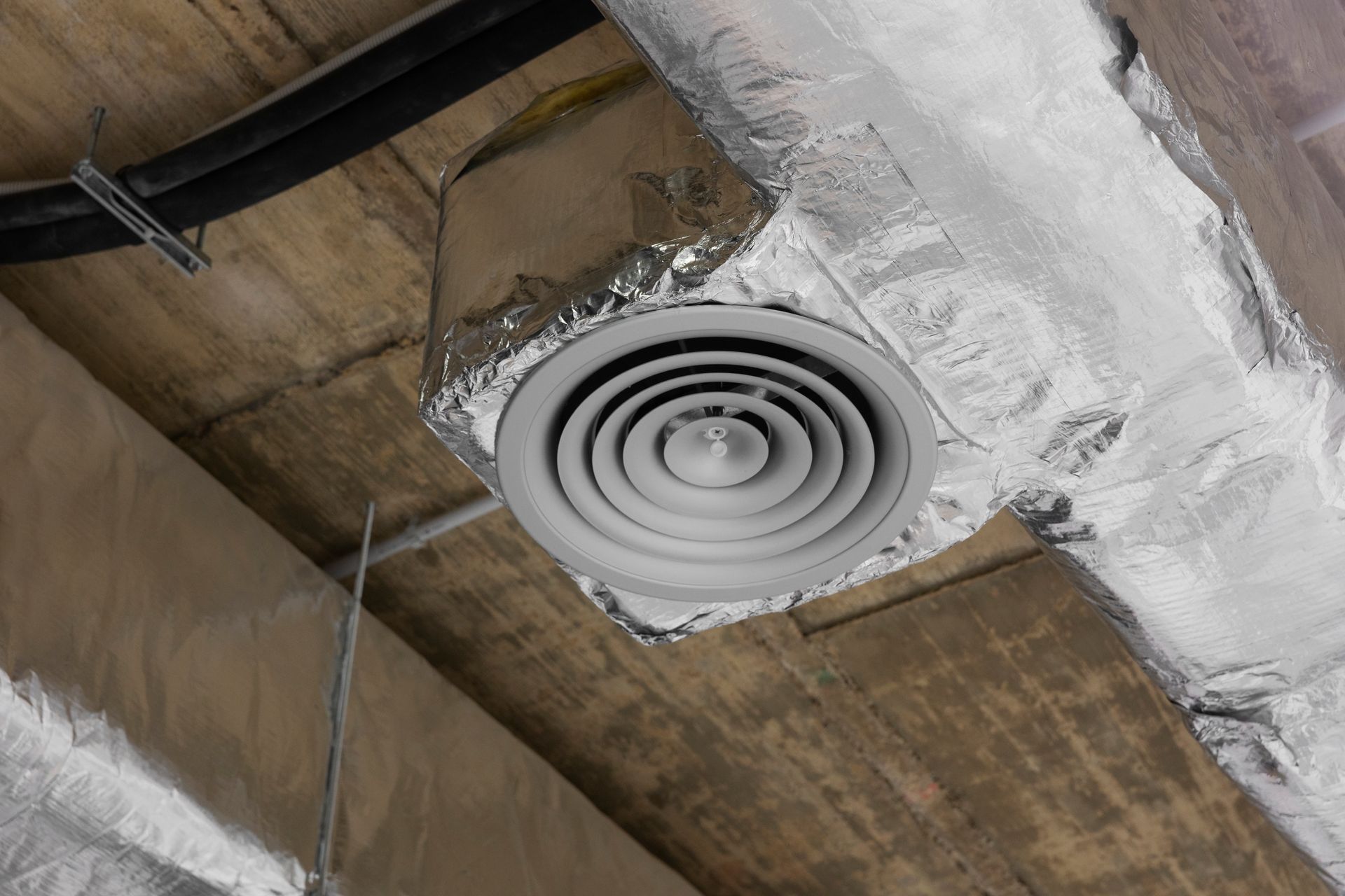 Ceiling air vent with circular grille in an unfinished concrete interior