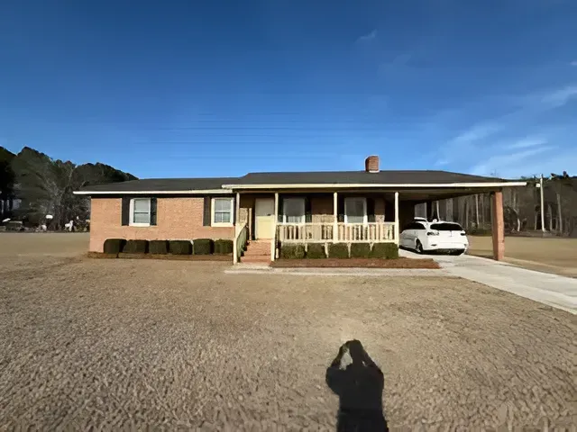 Single-story brick house with a front porch and a white car parked in the driveway