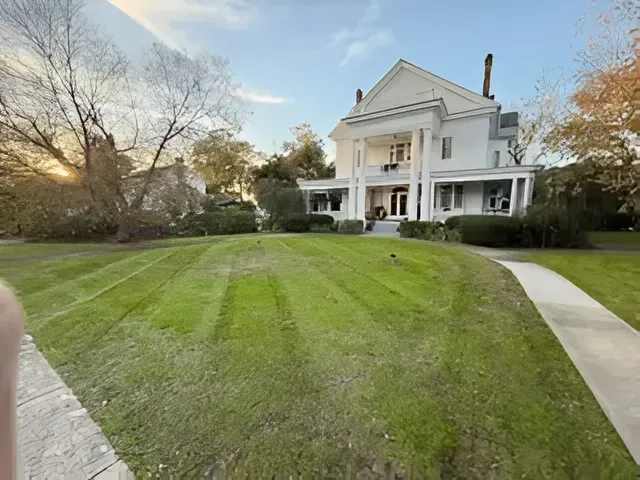 Large white farmhouse with wraparound porch on a grassy lawn at sunset