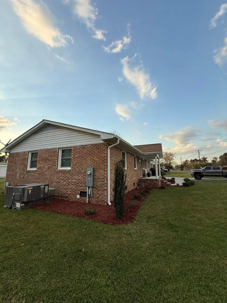 Brick house with white trim and red landscaping beside a grassy yard under a partly cloudy sky