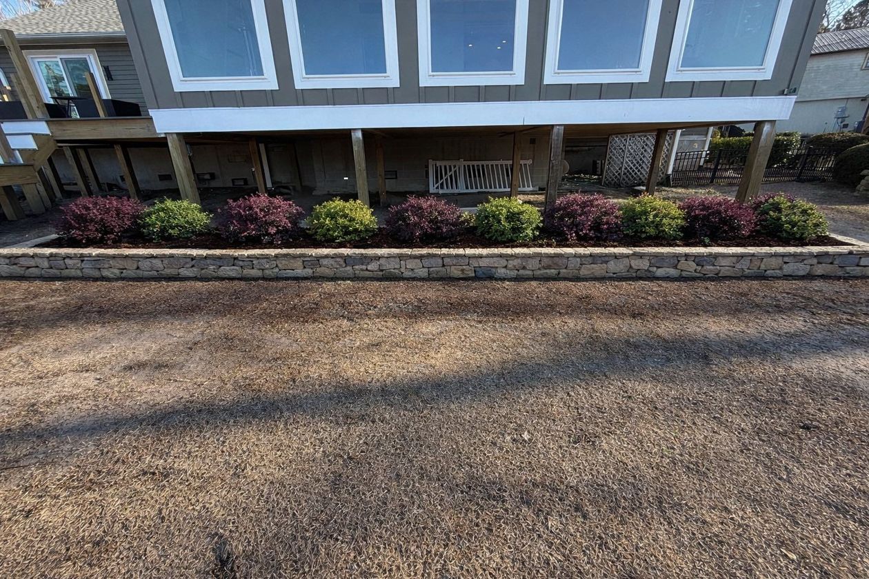 Apartment building facade with blue trim, flower bed, and gravel parking area in front