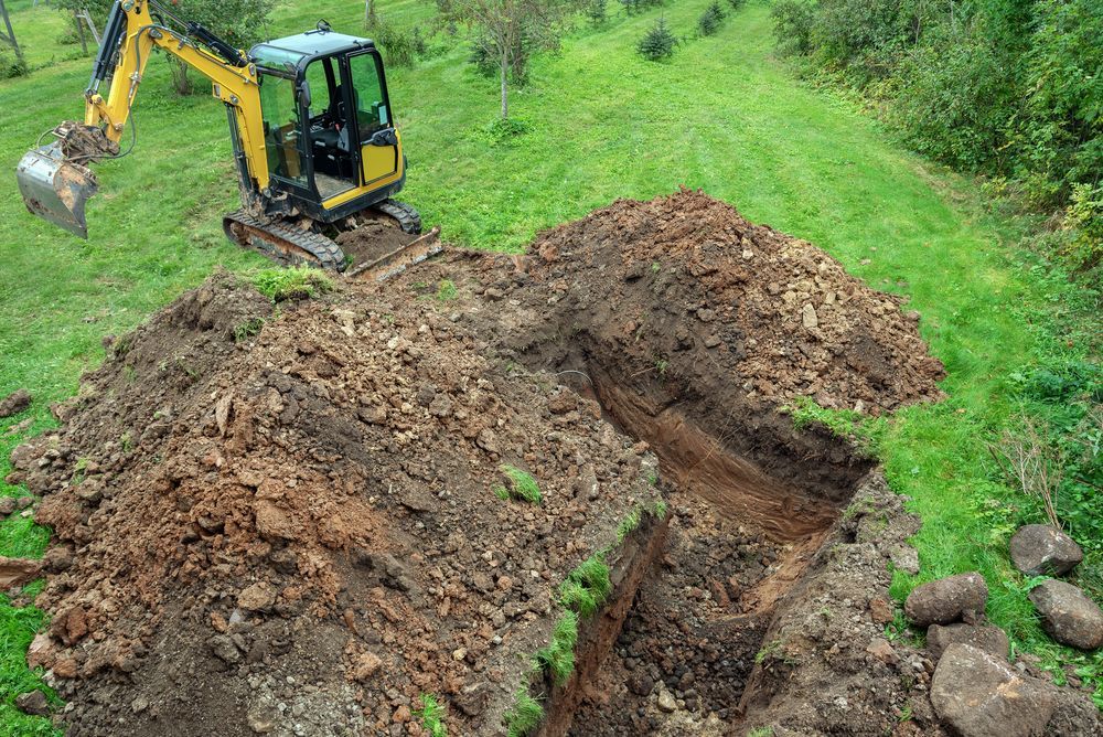 Yellow excavator digging a large dirt trench on a grassy hillside