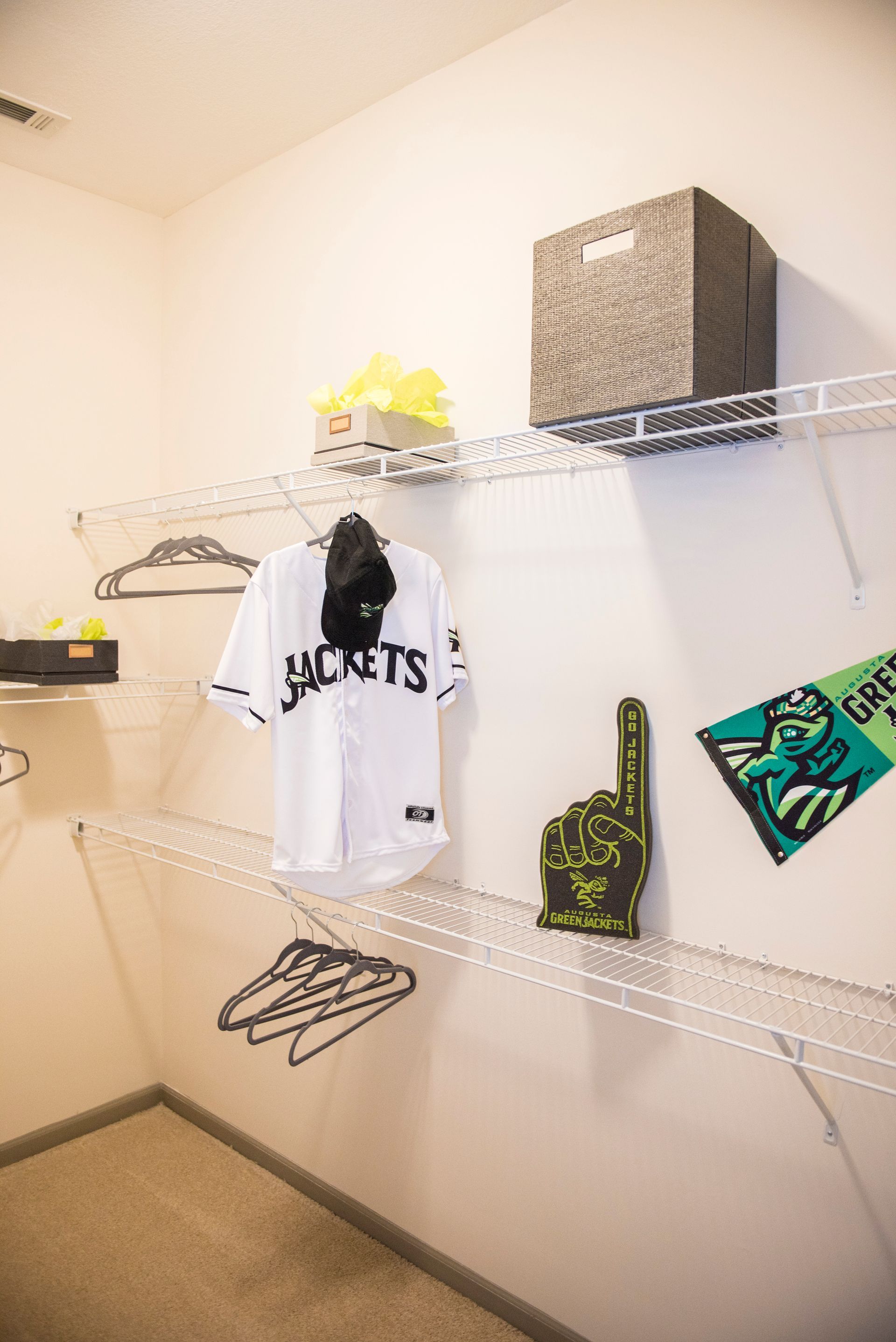 Closet with wire shelving holding a jersey, hat, and fan gear. White walls, beige carpet at Ironwood Apartment Homes.