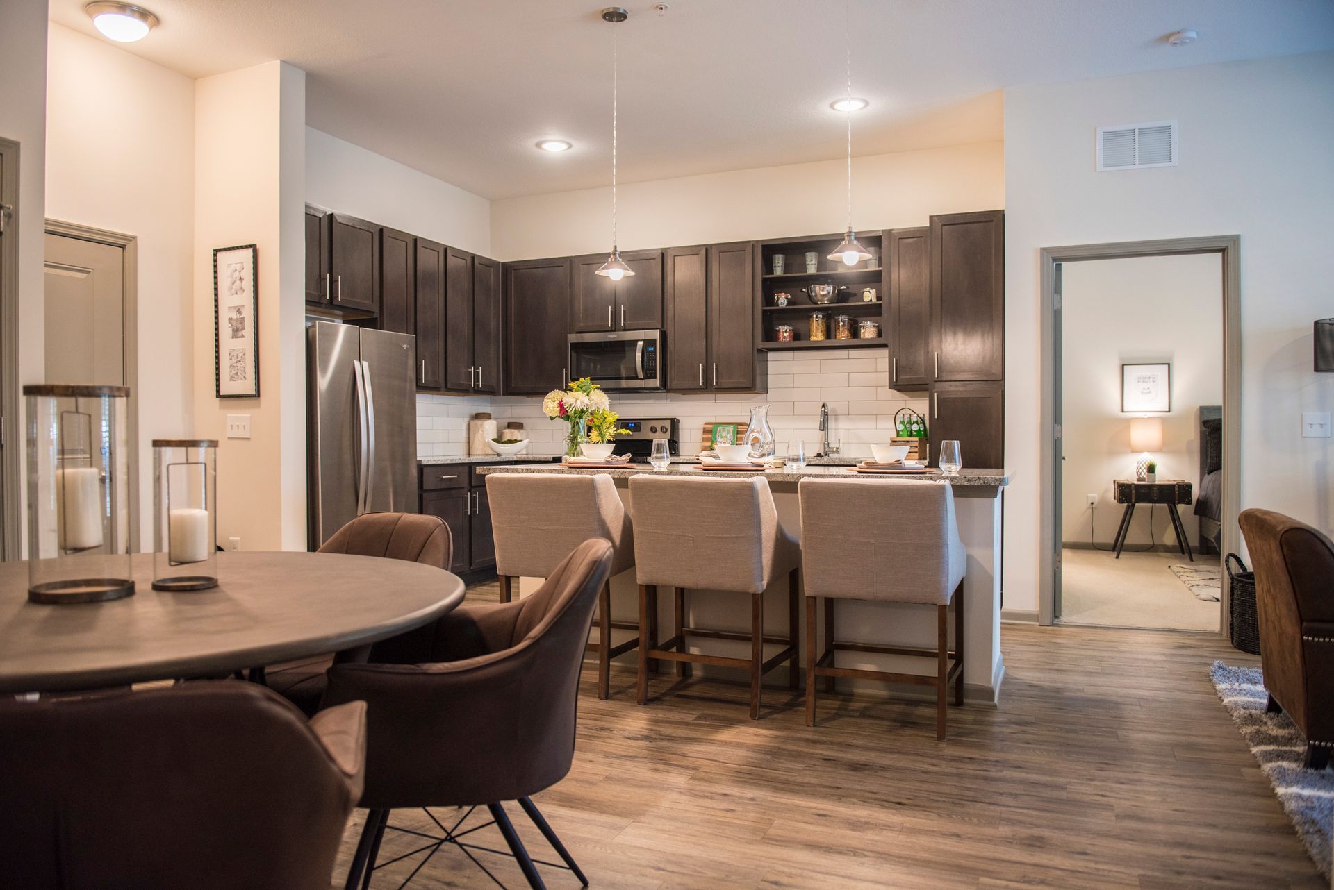 Open-concept kitchen and dining area: dark cabinetry, stainless steel appliances, neutral tones, island seating, round dining tables at Ironwood Apartment Homes.