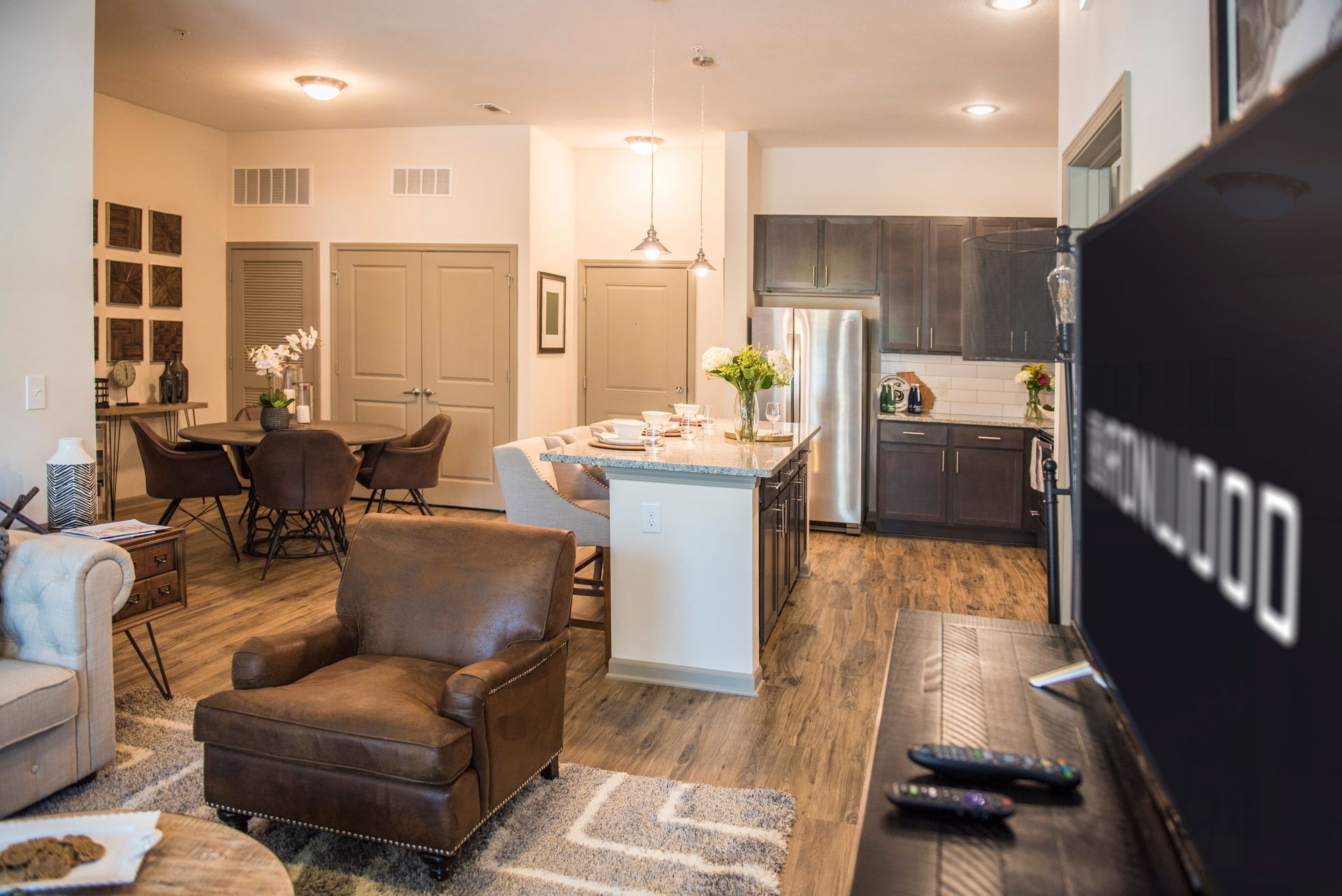 Open-concept apartment interior with living, dining, and kitchen areas. Features include brown leather chair, island, stainless appliances at Ironwood Apartment Homes.