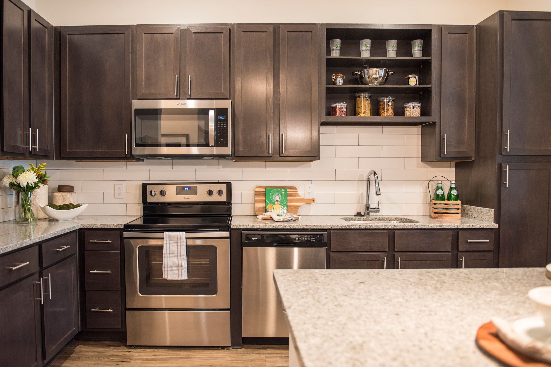 Dark wood kitchen with stainless steel appliances, granite countertops, and open shelves at Ironwood Apartment Homes.