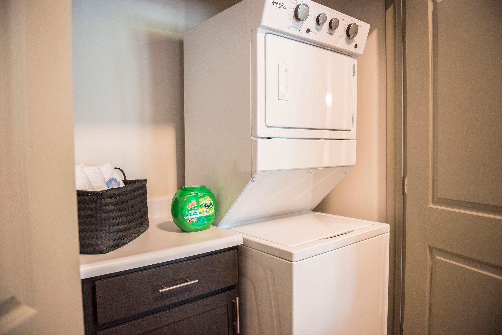 Stacked white washer and dryer in a laundry area, with laundry basket and detergent pod at Ironwood Apartment Homes.