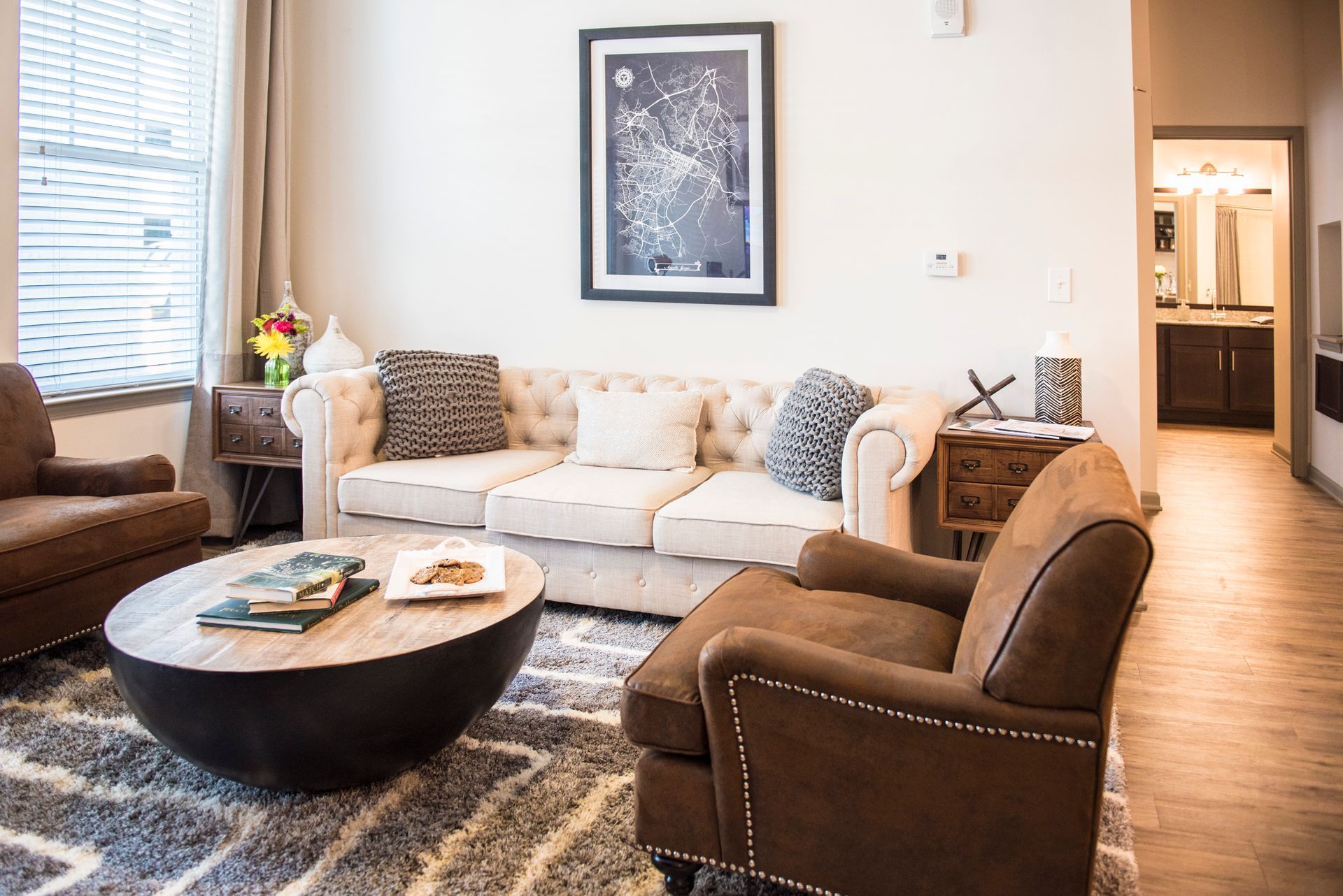 Living room with a beige tufted couch, brown chairs, and a round coffee table on a gray rug at Ironwood Apartment Homes.
