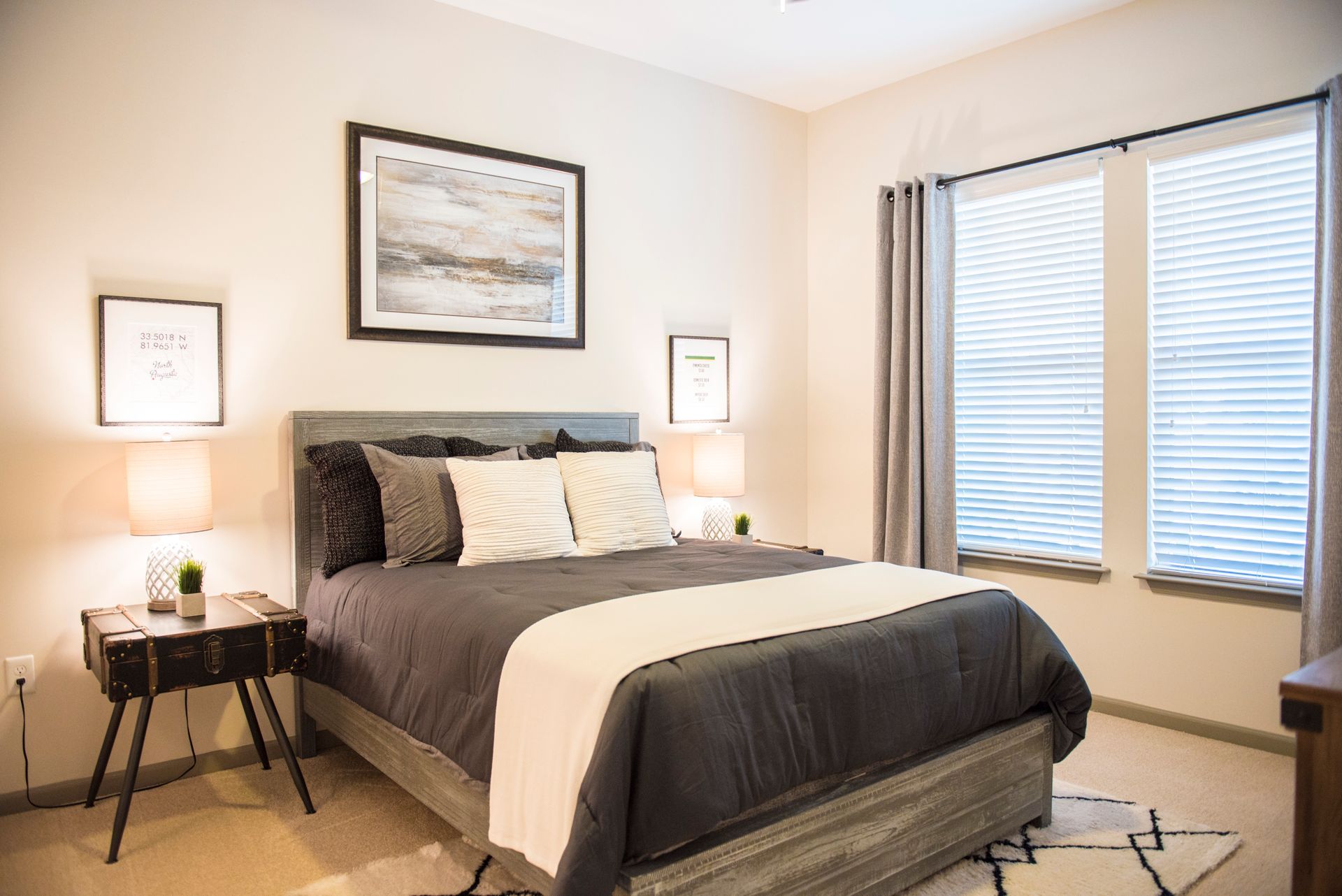 Bedroom with a gray bed, white and gray decor, and two bedside lamps at Ironwood Apartment Homes.