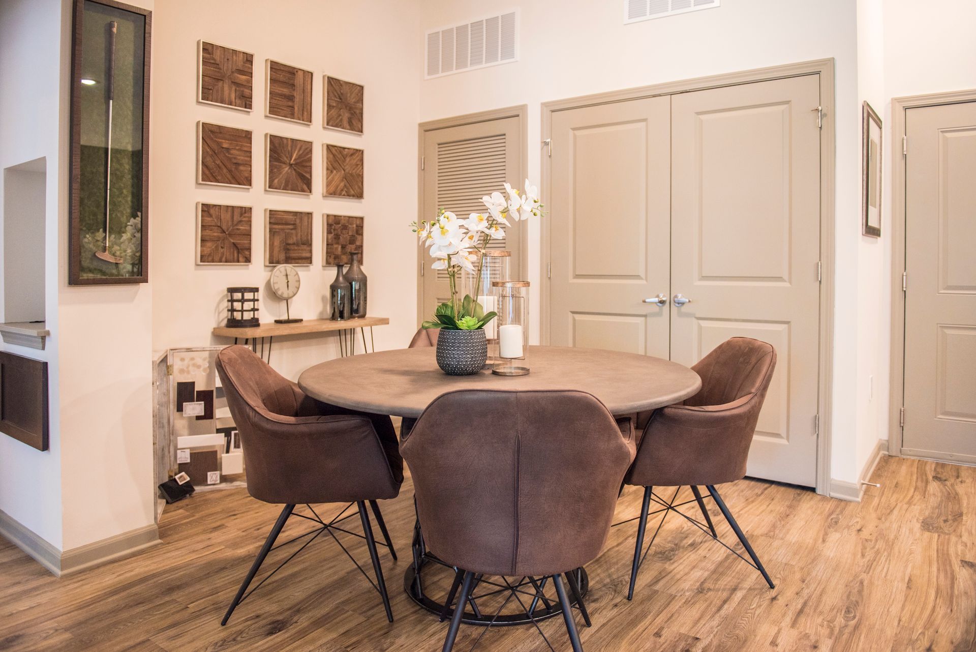 Dining area with round table, four brown chairs, decorative wall art, and flowers at Ironwood Apartment Homes.