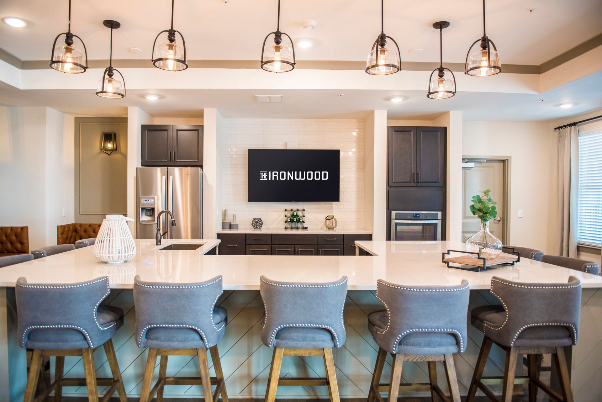 Kitchen with large island, pendant lights, bar stools, and entertainment area with TV at Ironwood Apartment Homes.