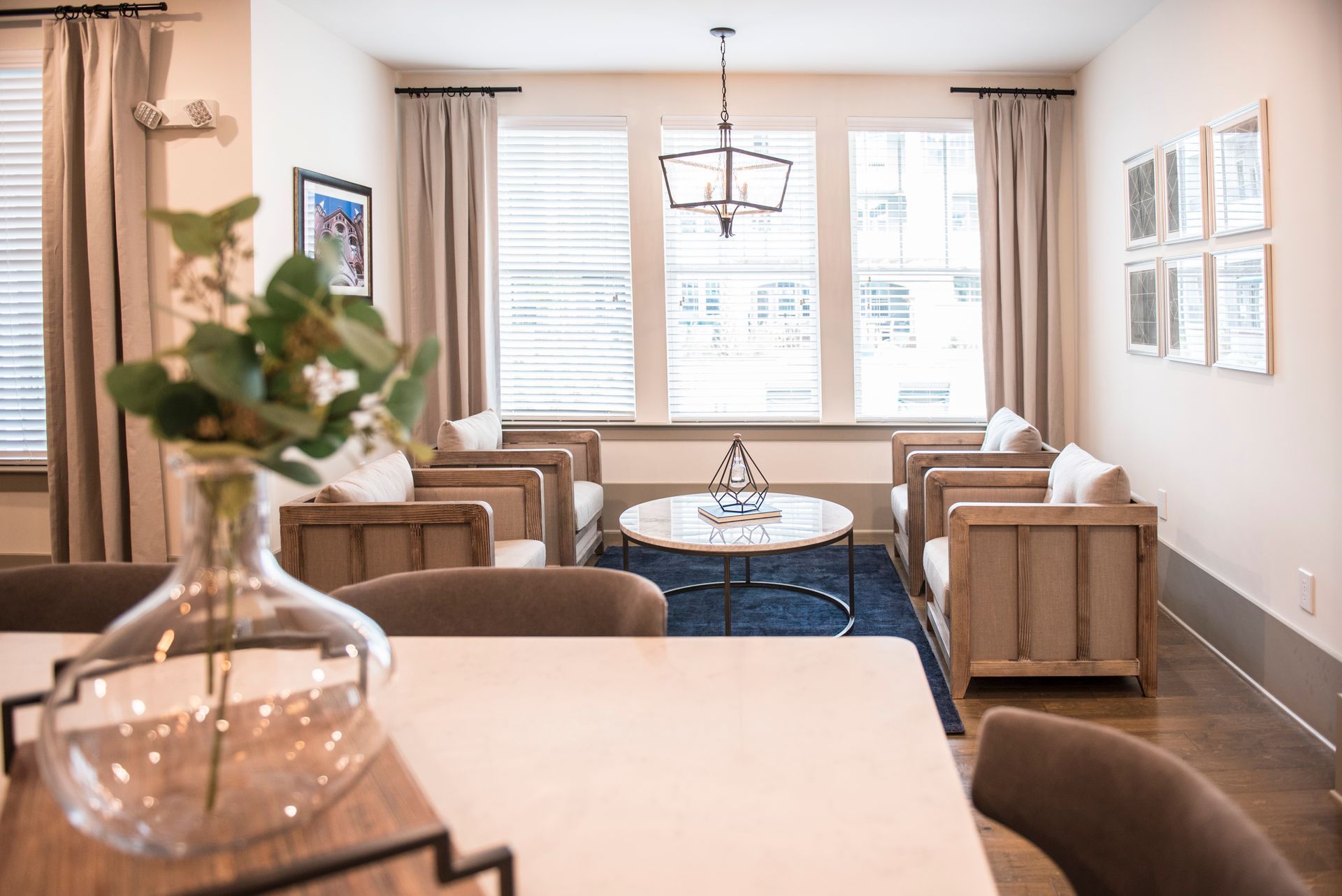 Living room with neutral tones, wood furniture, and a blue rug; a vase of greenery in the foreground at Ironwood Apartment Homes.