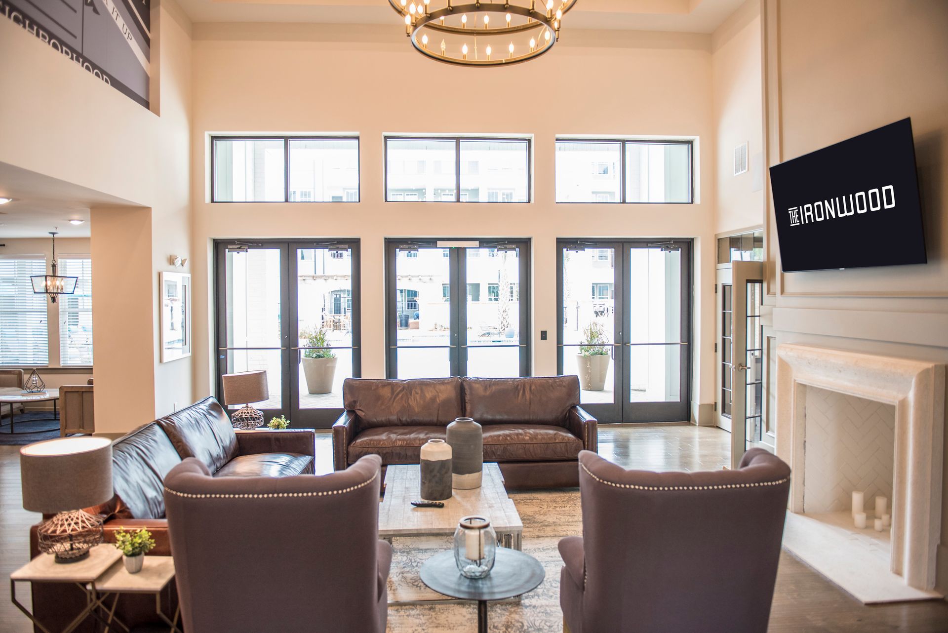 Lobby with seating, fireplace, and television. Large windows and doors lead to the outside at Ironwood Apartment Homes.