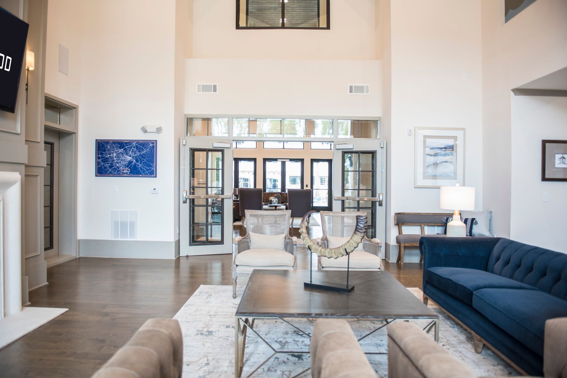 Spacious lobby with blue sofa, armchairs, coffee table, art, and doors to an exterior at Ironwood Apartment Homes.