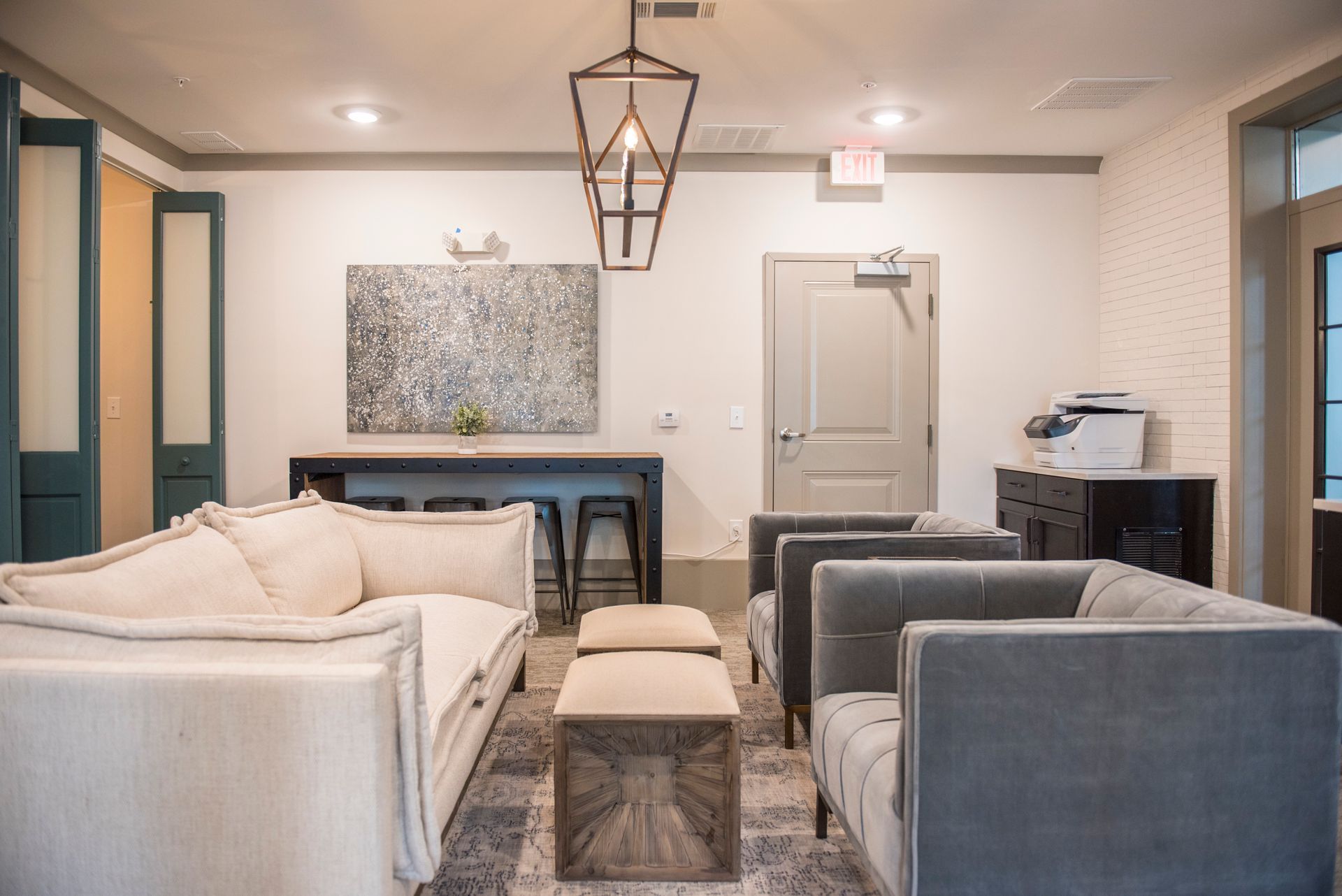 Cozy lounge area with two sofas, stools, a high-top table, and a decorative light fixture at Ironwood Apartment Homes.
