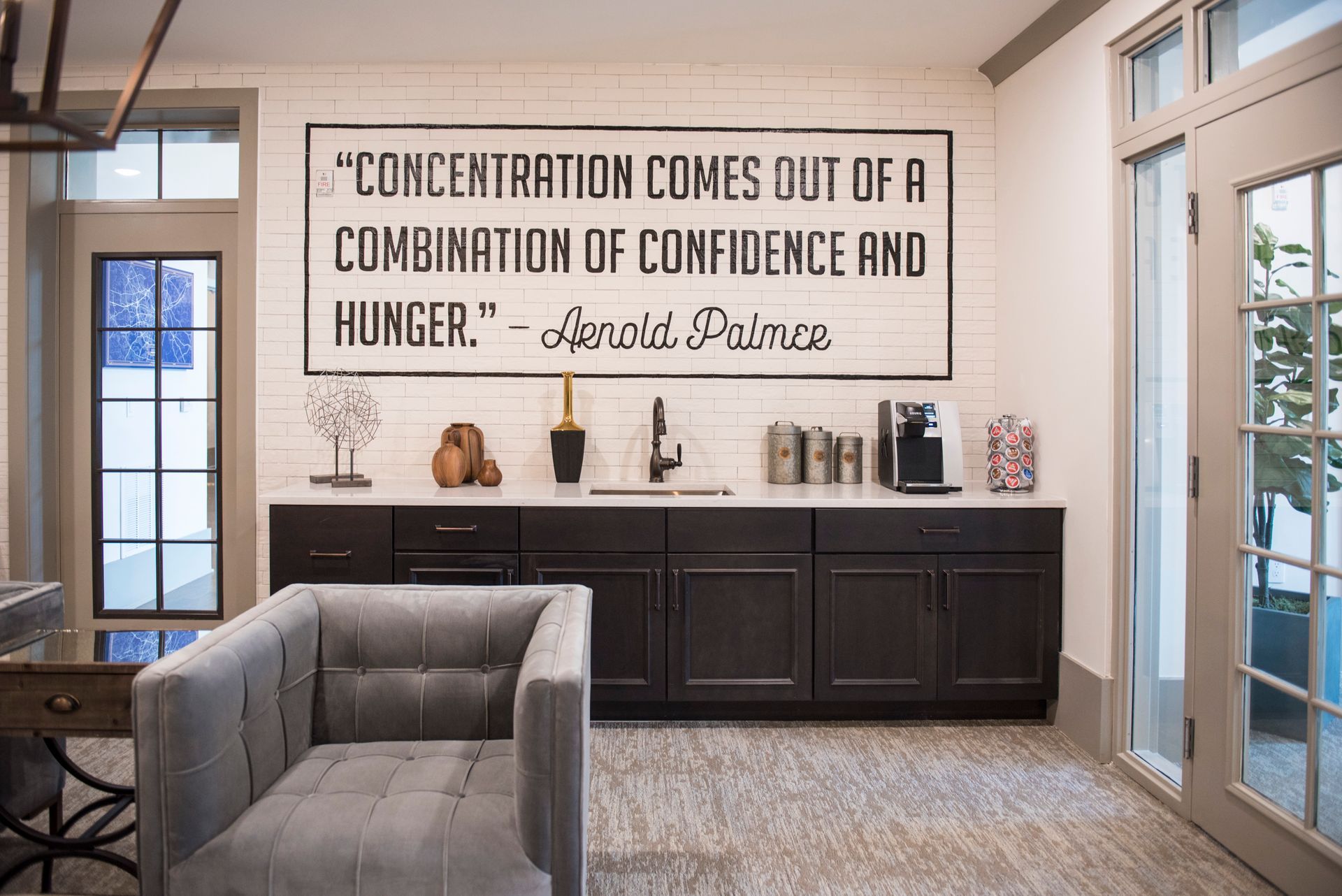 A room with a coffee bar, gray armchair, and a sign with a quote by Arnold Palmer at Ironwood Apartment Homes.