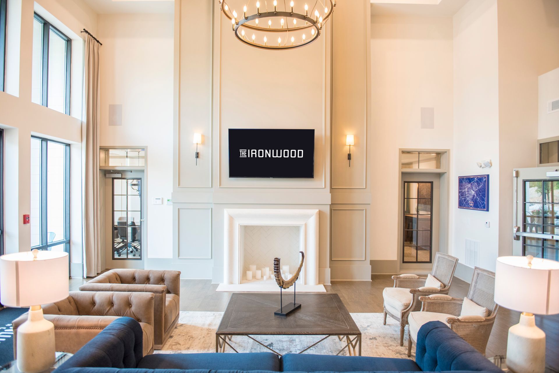Lobby with seating, fireplace, and TV. Neutral colors, modern design. The Fox Wood logo is displayed on the TV at Ironwood Apartment Homes.