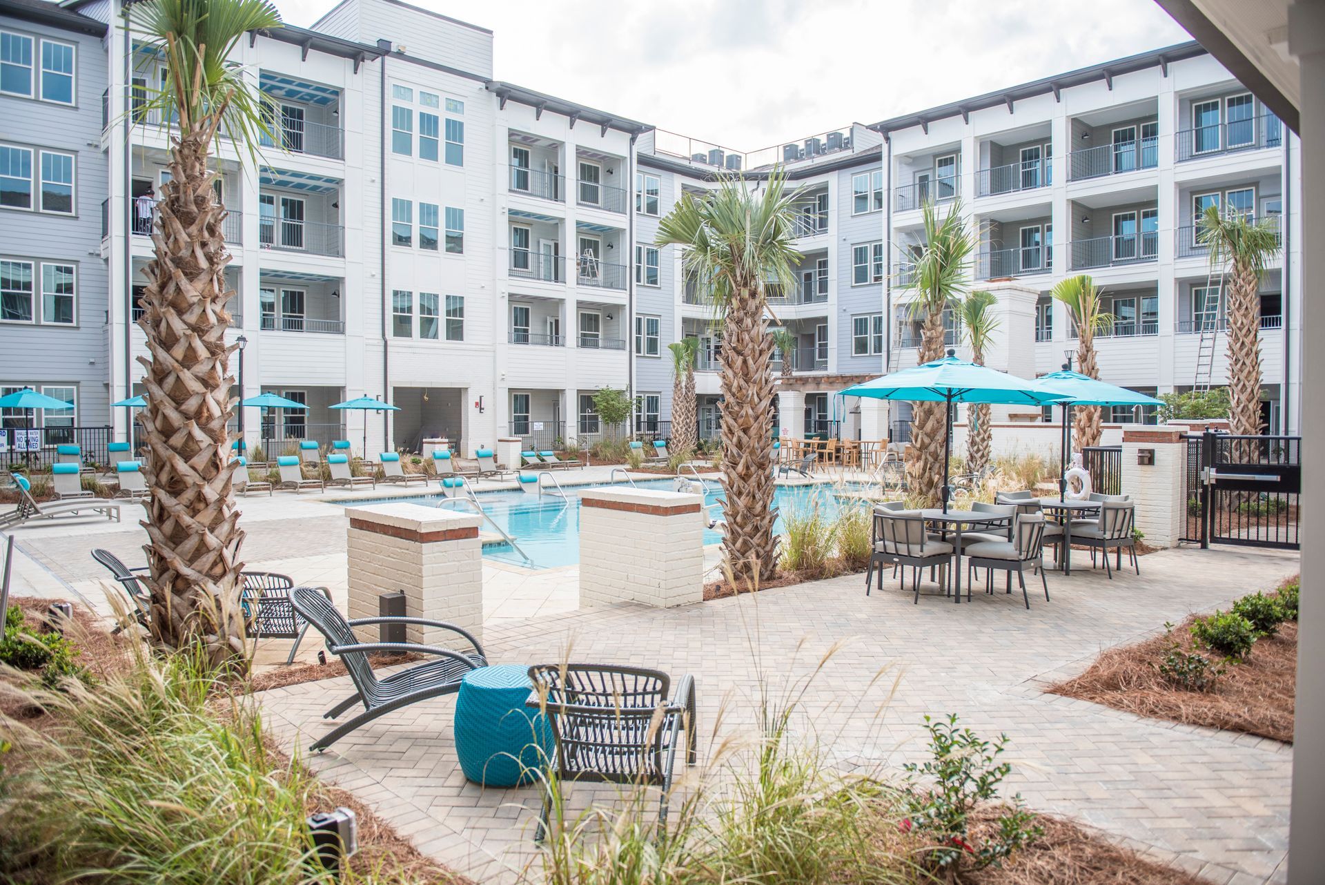Pool area with lounge chairs, tables, and palm trees, surrounded by white apartment buildings at Ironwood Apartment Homes.