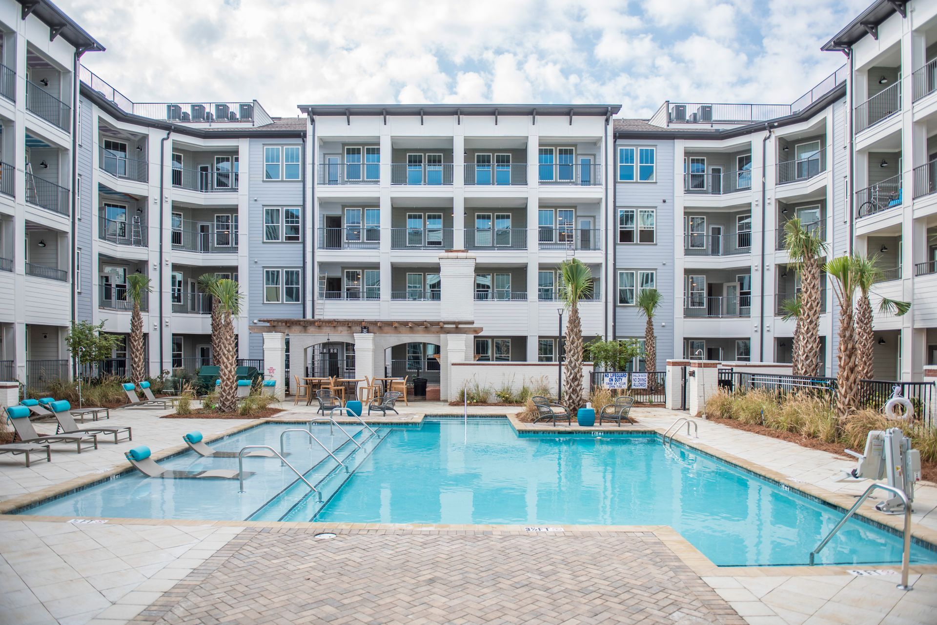 Apartment complex with a pool. Buildings are white with balconies. Pool has lounge chairs and palm trees at Ironwood Apartment Homes.