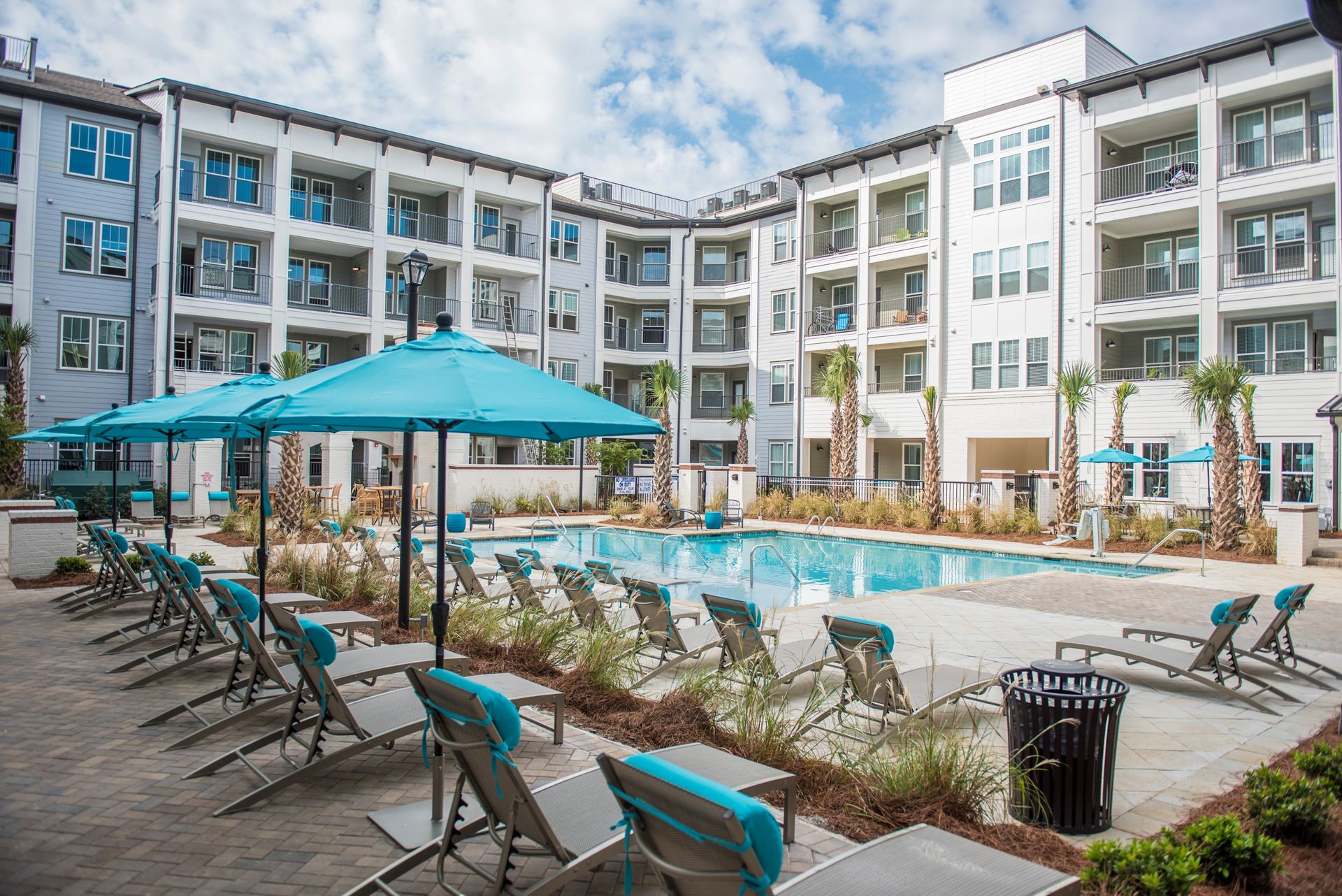 Pool area with lounge chairs, blue umbrellas, and a multi-story apartment building at Ironwood Apartment Homes.