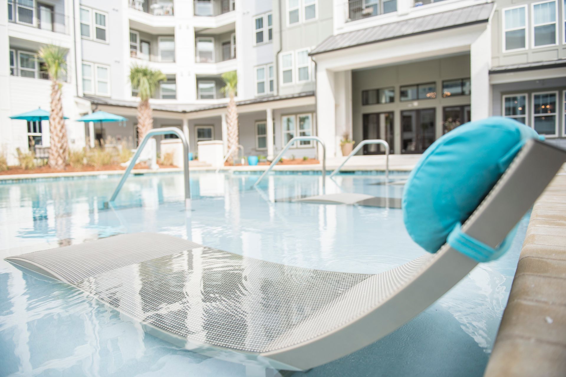 Lounge chair with turquoise pillow by a pool at an apartment complex at Ironwood Apartment Homes.