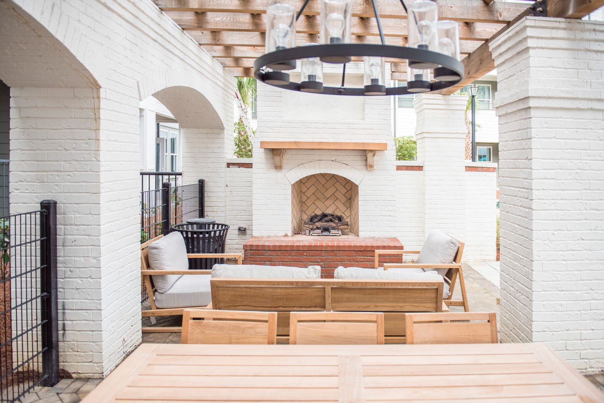 Outdoor patio with white brick, fireplace, wooden furniture, and black chandelier at  Ironwood Apartment Homes.