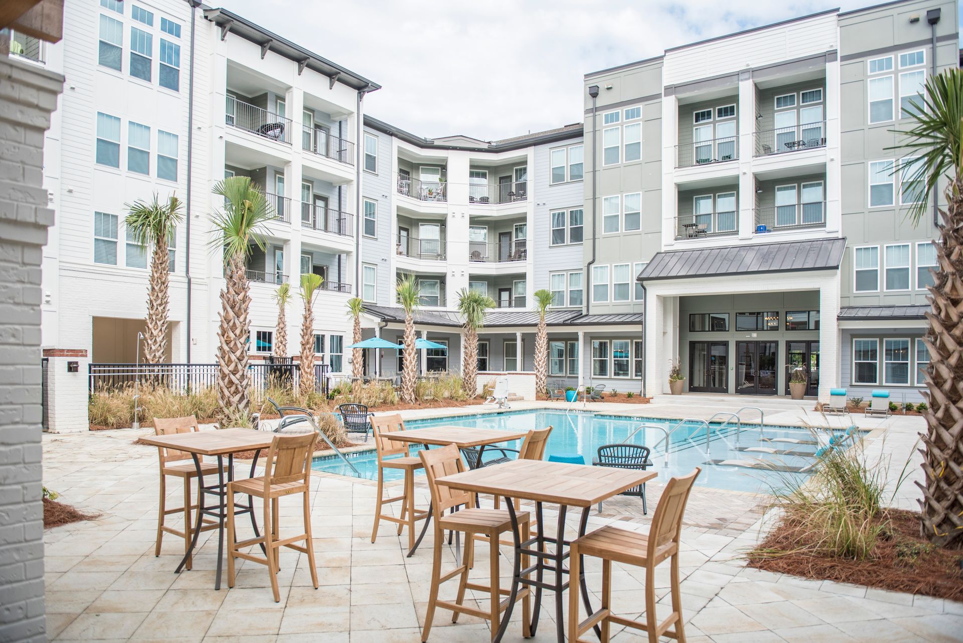 Outdoor pool area with tables, chairs, and multiple story apartment buildings at Ironwood Apartment Homes.