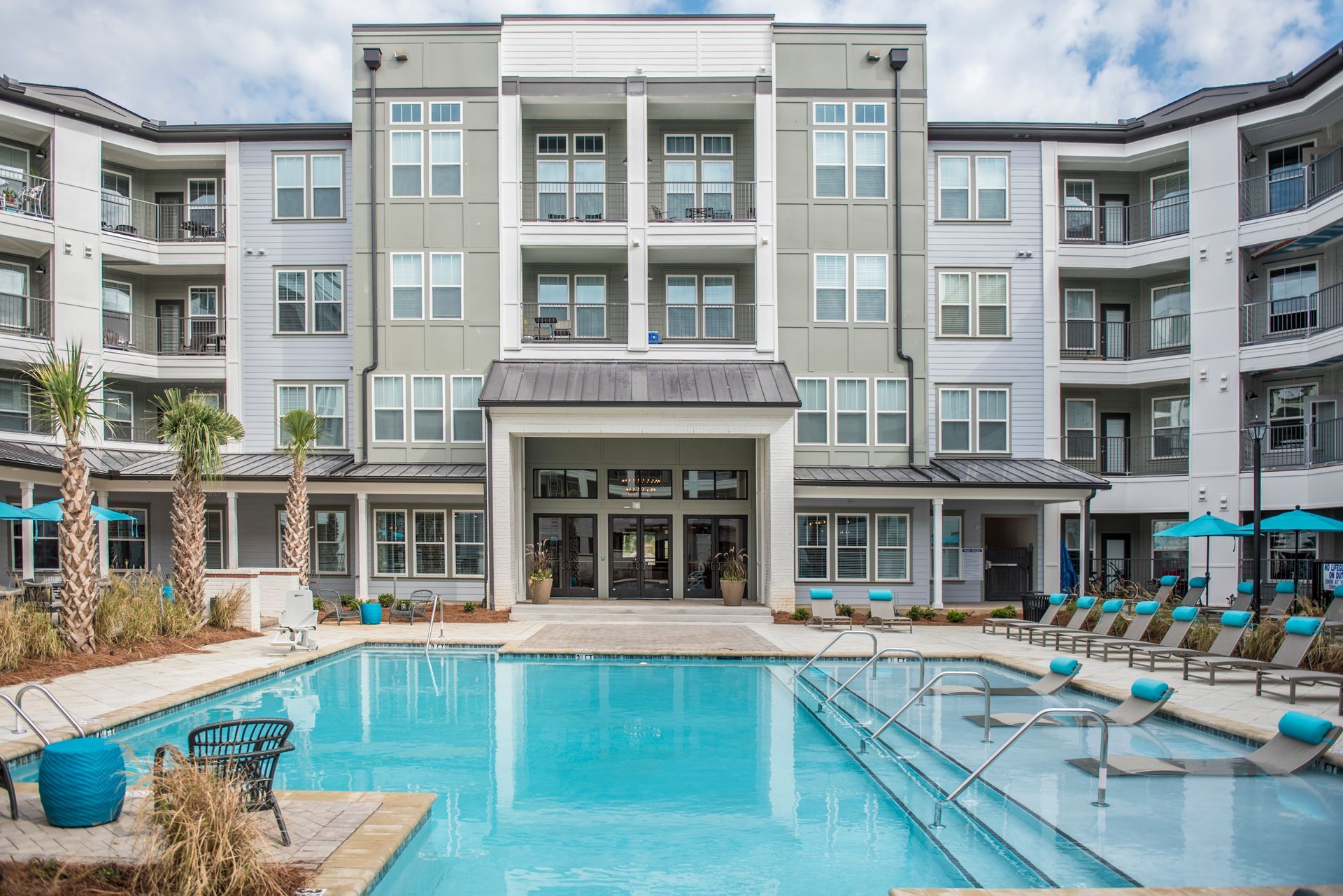 Apartment building with pool. Exterior view: grey building, turquoise pool, lounge chairs, blue umbrellas at Ironwood Apartment Homes.