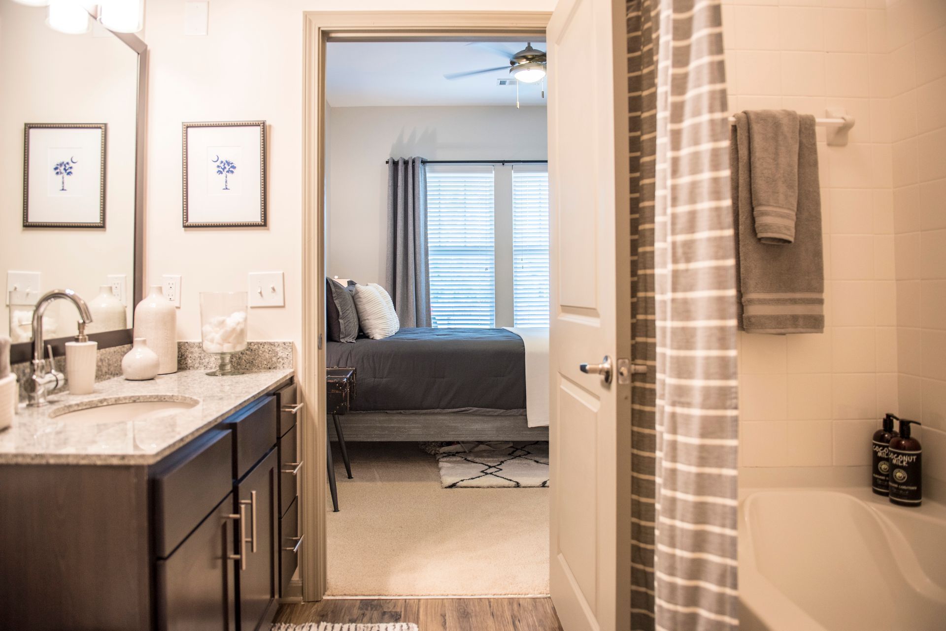 Bathroom doorway leads to bedroom with grey bedding. White walls, grey accents at Ironwood Apartment Homes.