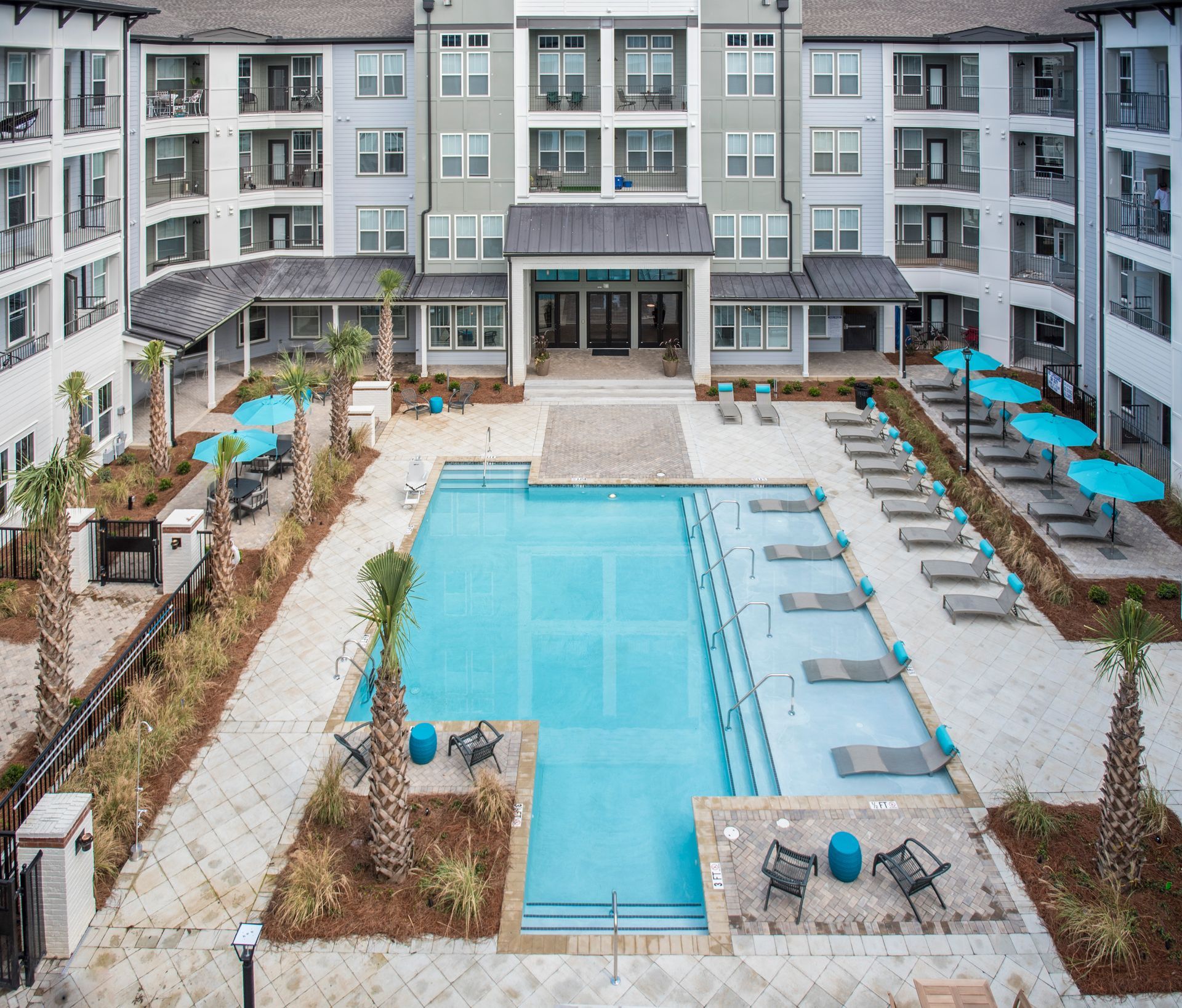 Aerial view of apartment complex with pool; light blue water, lounge chairs, and palm trees at  Ironwood Apartment Homes.