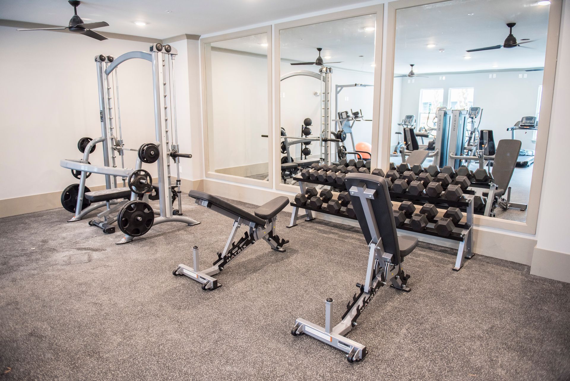 Gym with weight machines, dumbbells, and adjustable benches reflected in wall mirrors at Ironwood Apartment Homes.