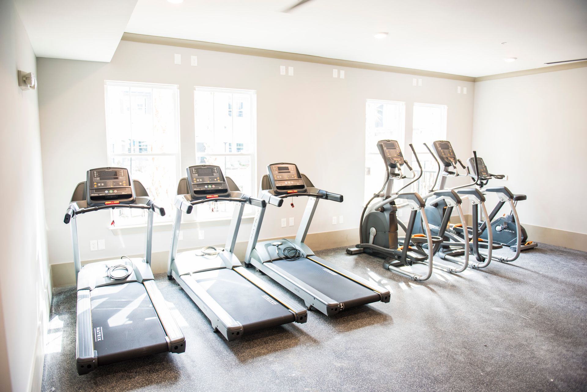 Gym with three treadmills and two elliptical machines by a window at  Ironwood Apartment Homes.