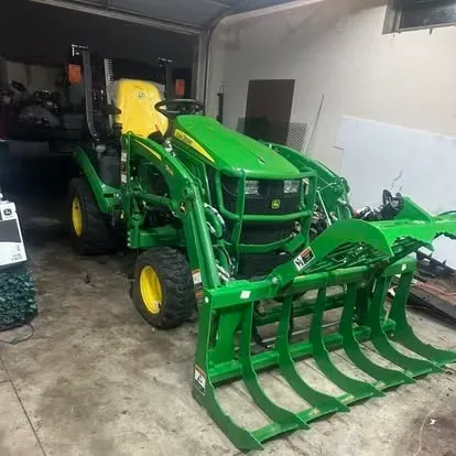 Green John Deere tractor with front grapple bucket parked in a garage