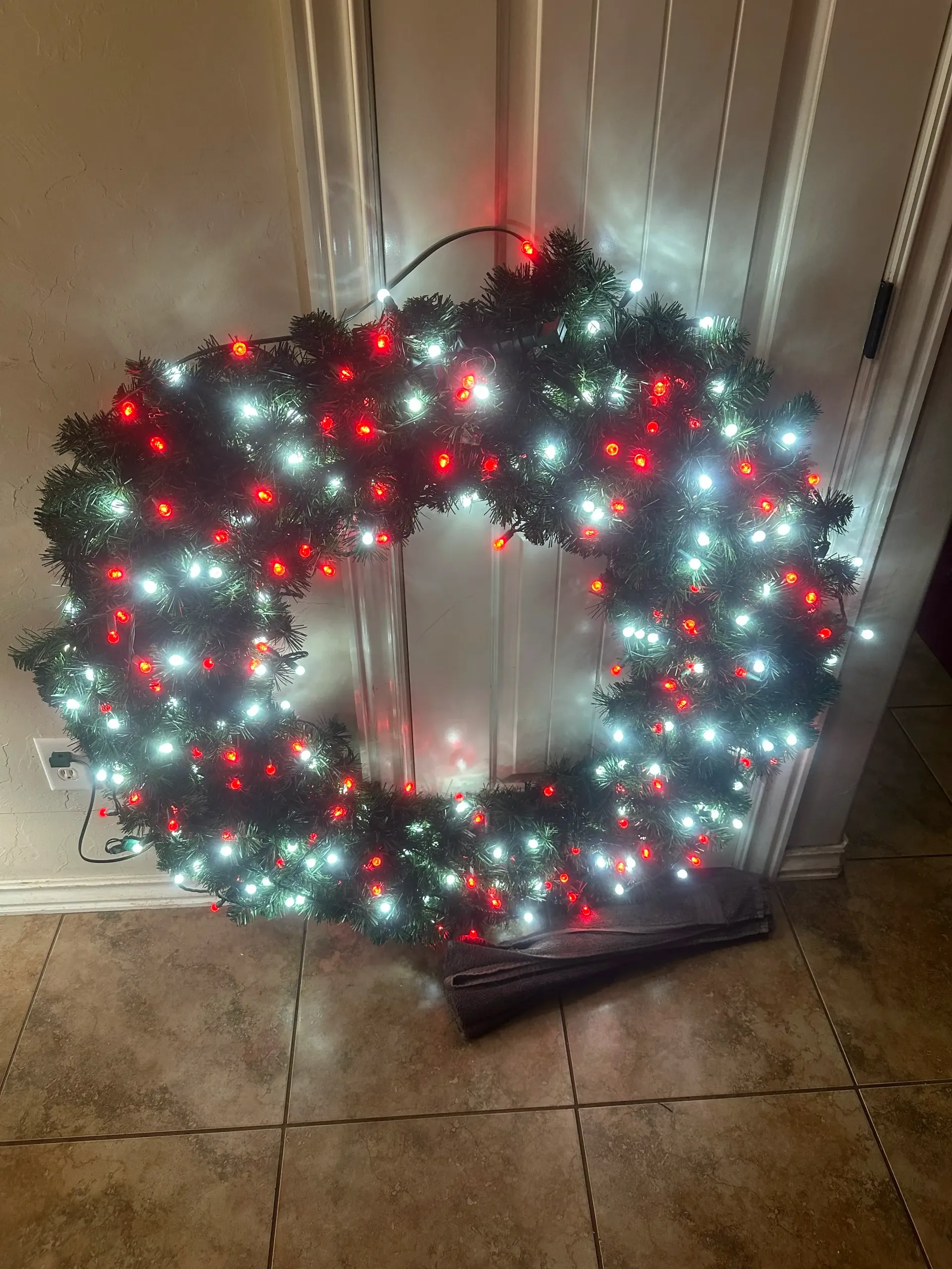Large green evergreen Christmas wreath by Campbell & Sons, illuminated with bright red and cool-white LED lights indoors.