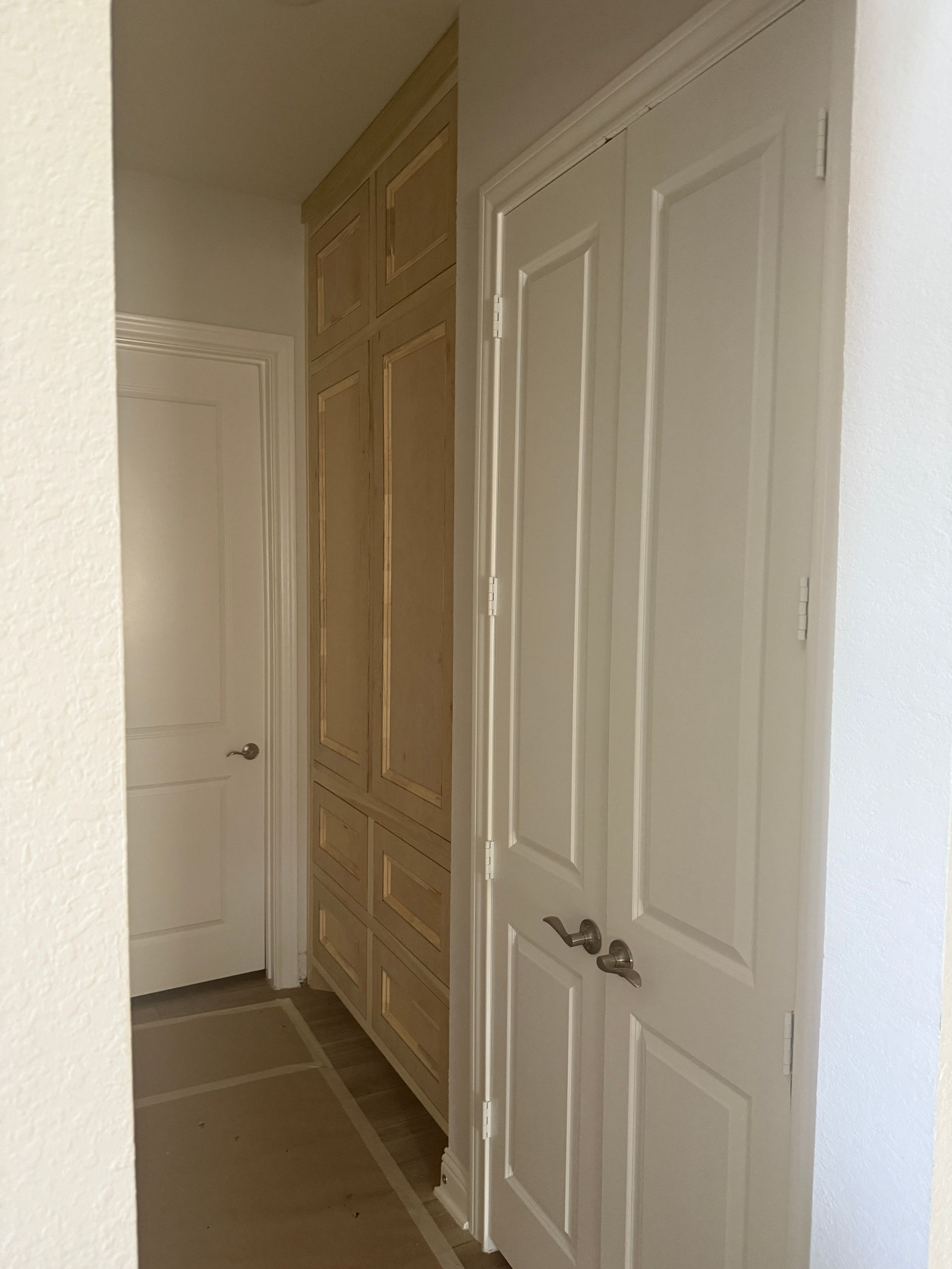 A close-up of a white bathroom vanity with two doors featuring a natural wood-toned center panel and decorative molding.