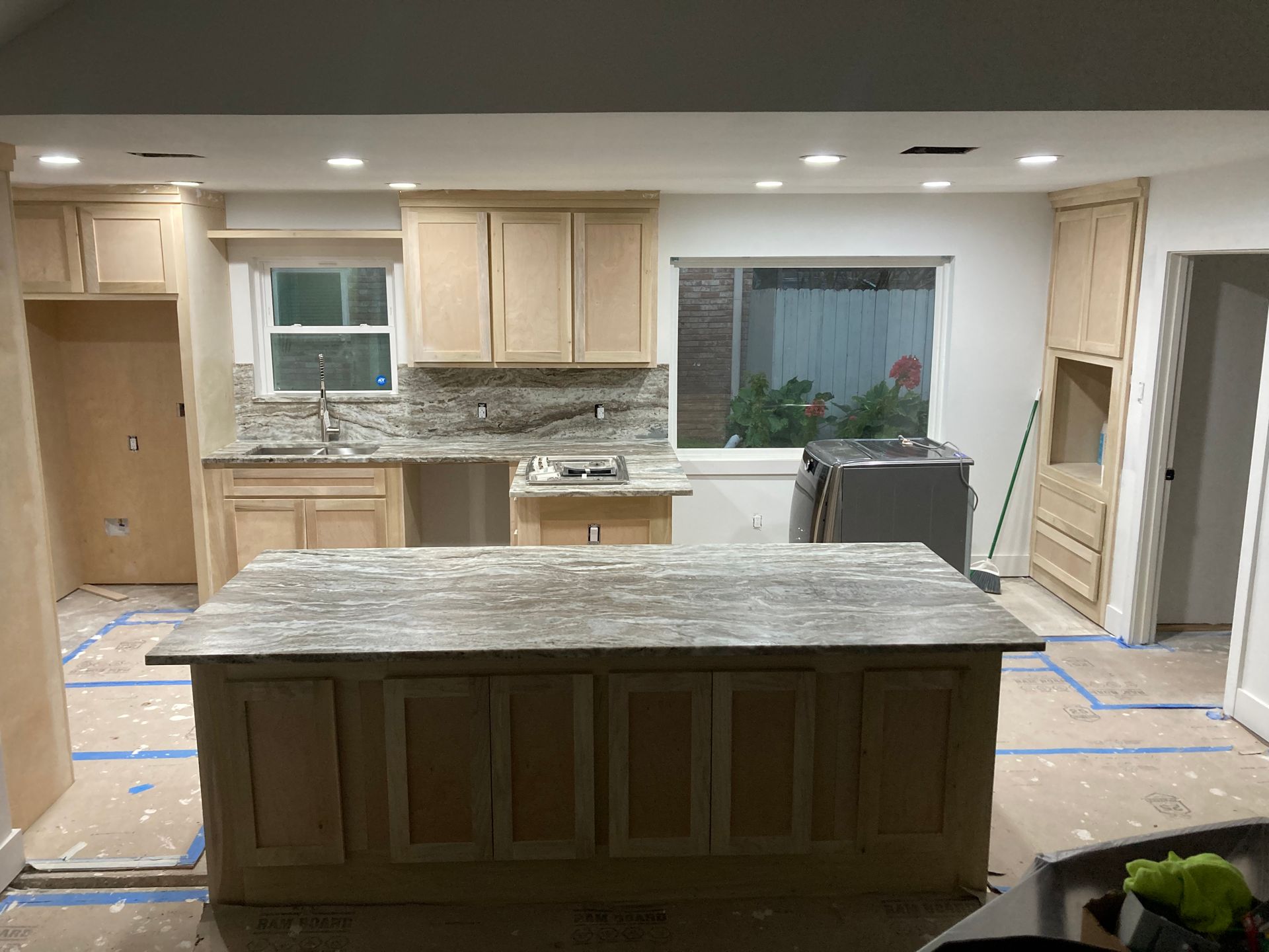 A kitchen with light wood cabinets, an island, a dining table with chairs, and tiled flooring.