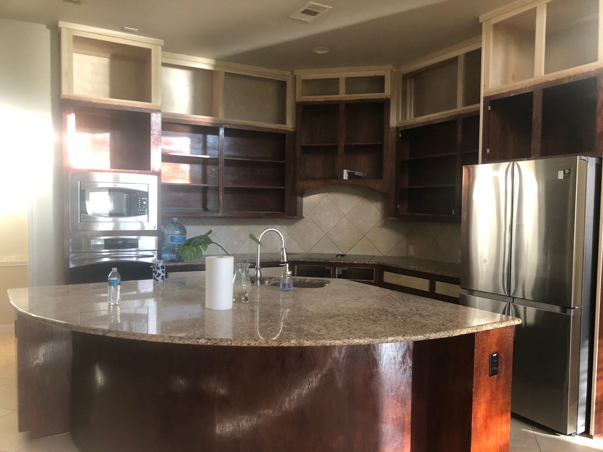 A kitchen with dark wood cabinets, a curved granite island, stainless steel appliances, and open upper shelving.