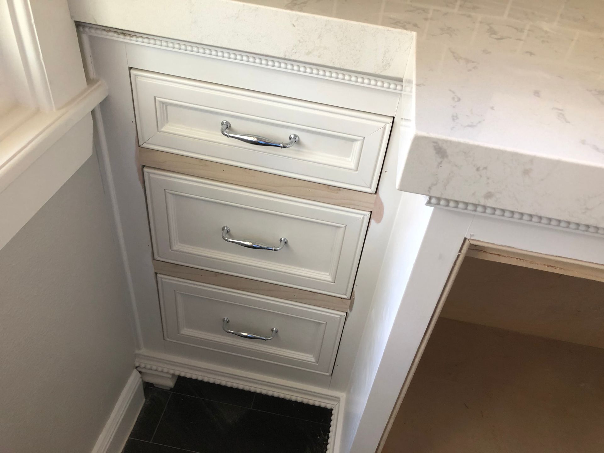 Three white, silver-handled drawers installed in a cabinetry unit beneath a white, marble-patterned countertop.